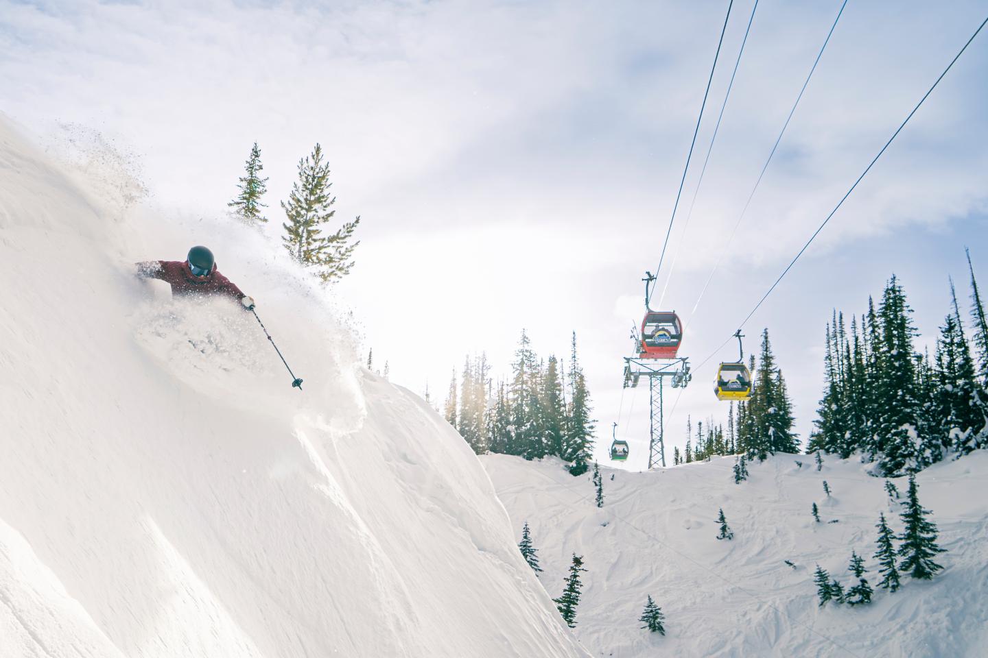 Skier carving down snowy slope, with gondolas in the background.