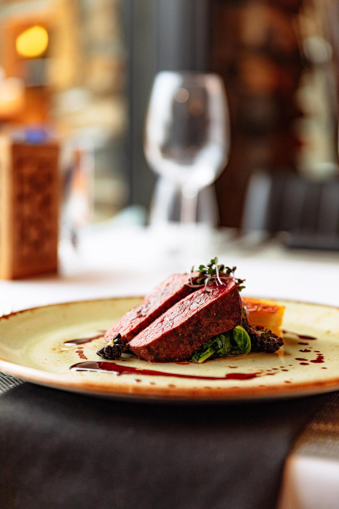 Seared steak slices on greens, elegant dining setting in the background.