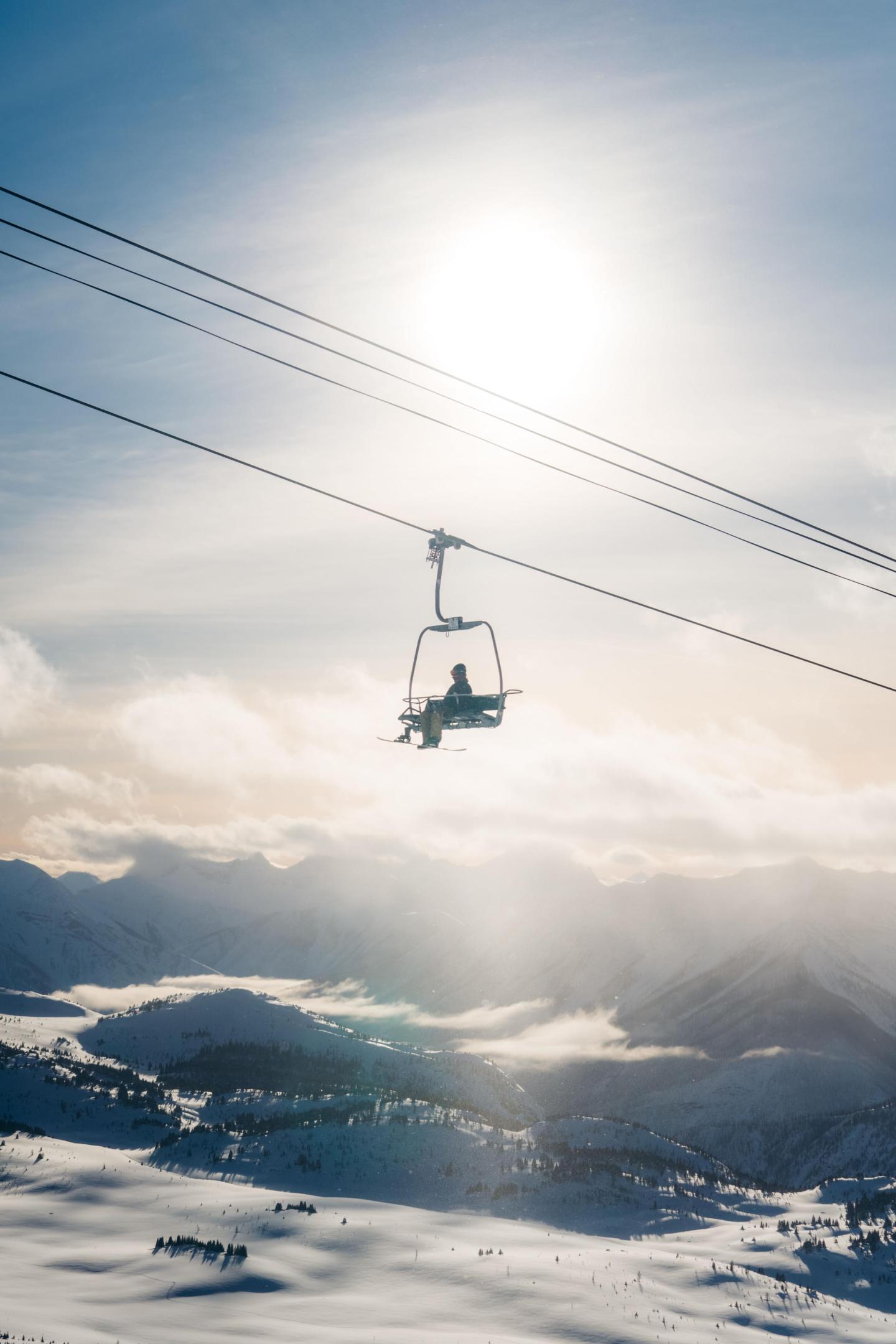 Ski lift ascending over snow-covered mountains, sun shining bright.