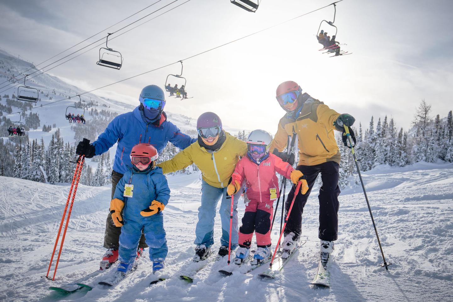 Family skiing on a snowy mountain, ski lifts in the background.
