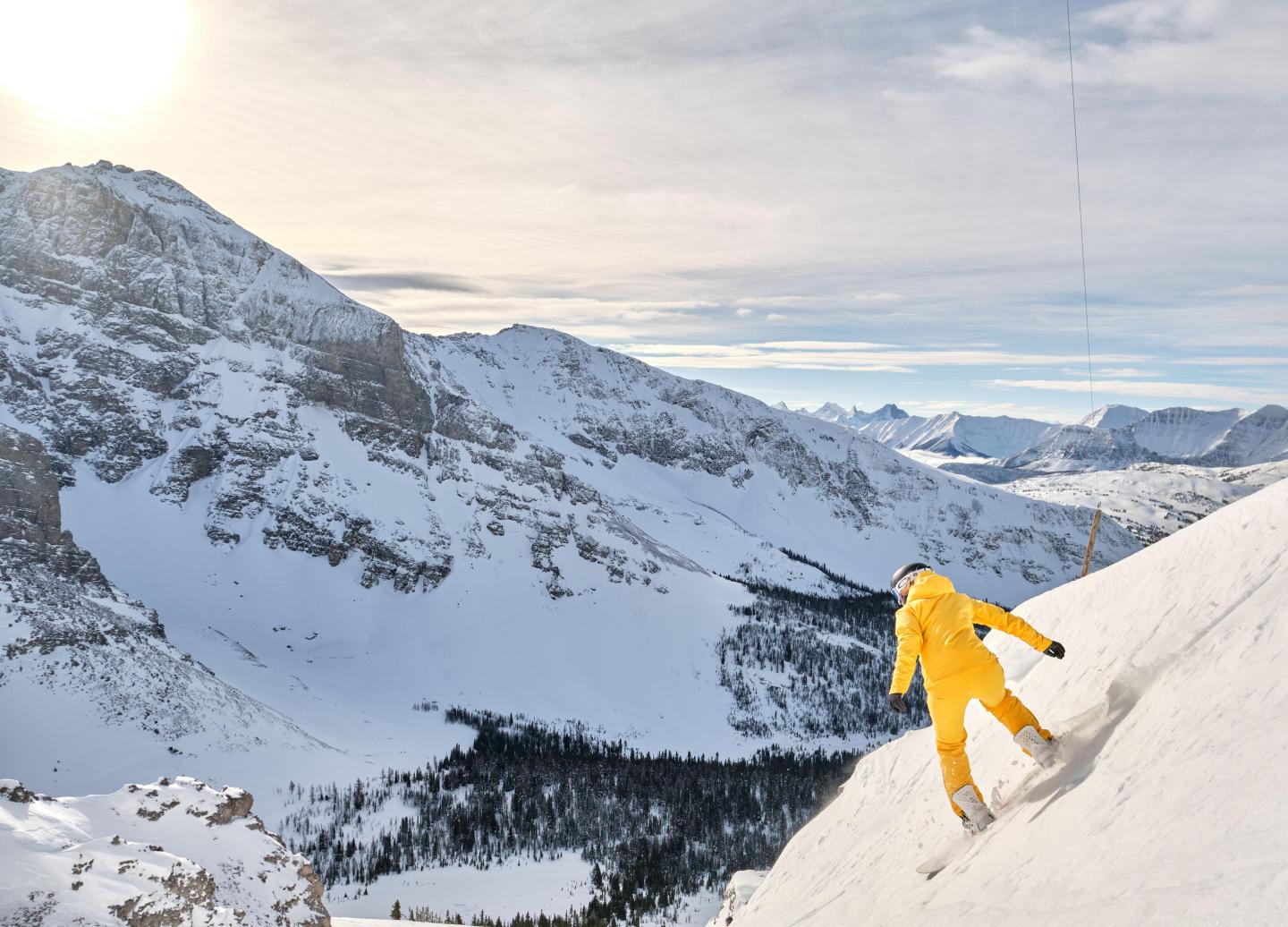 Skier in yellow descends snowy mountain under bright sun.