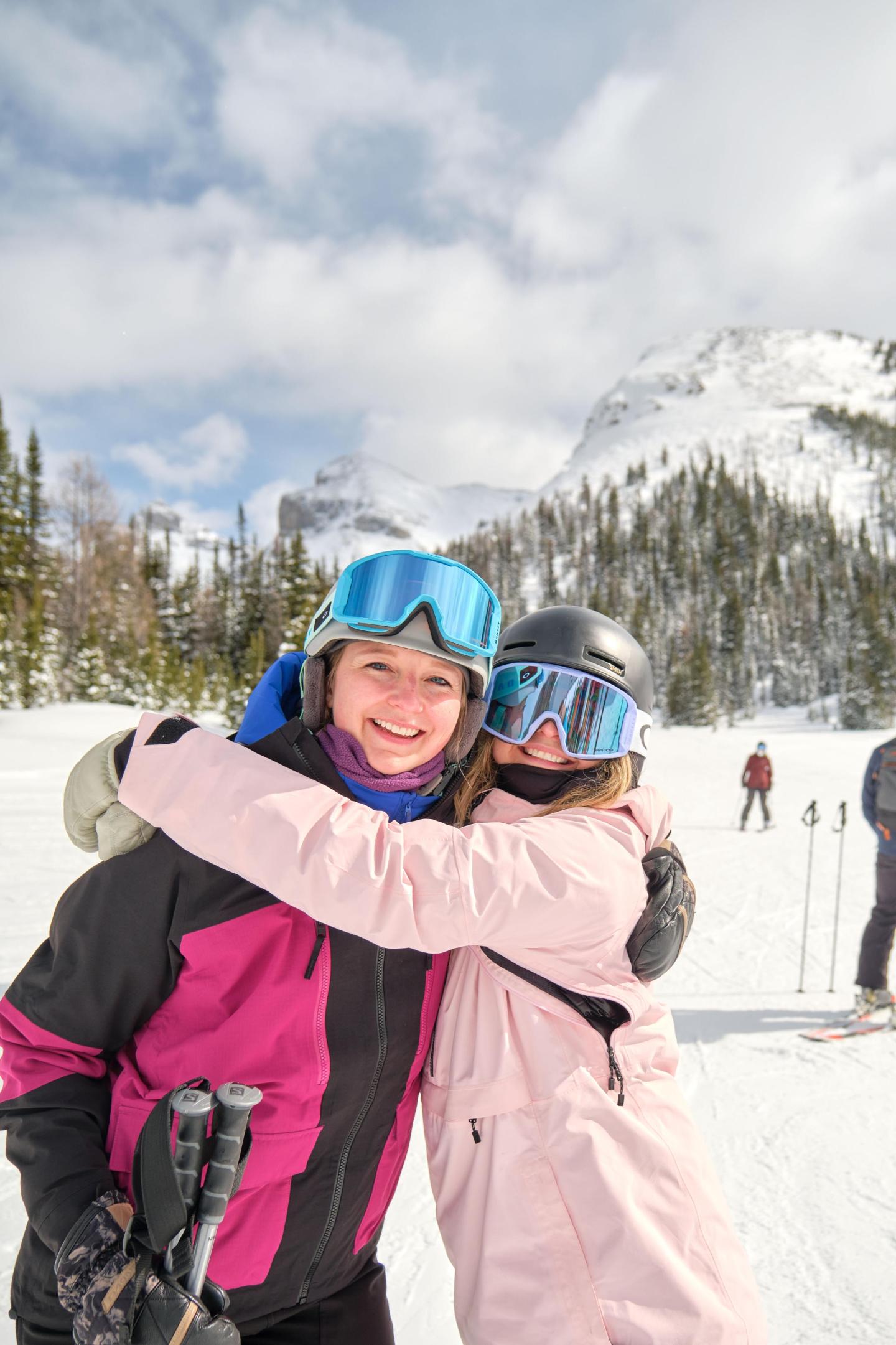 Two skiers smiling and hugging on a snowy mountain.