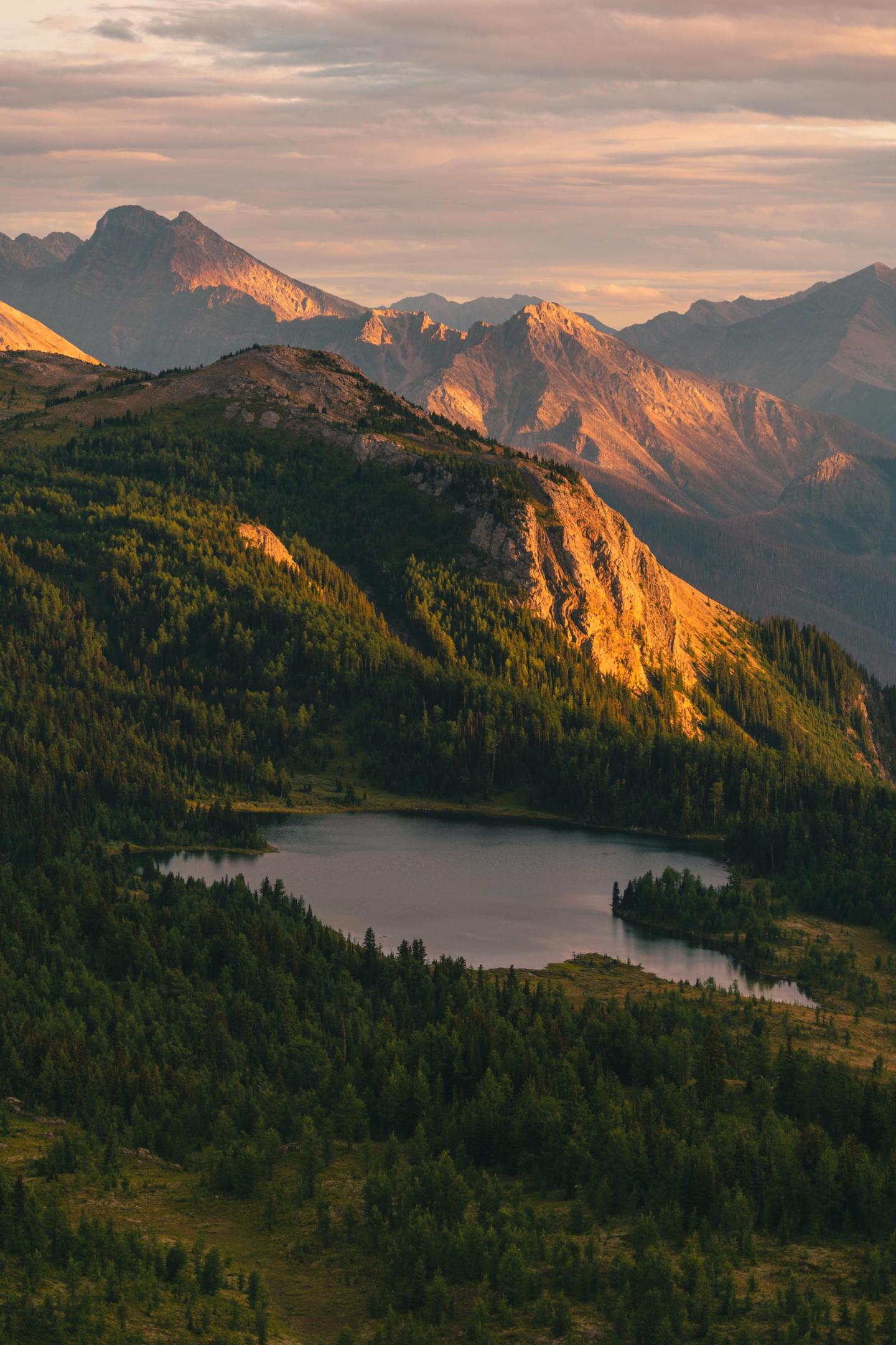 Mountain landscape at sunset with a lake and forest in the foreground.