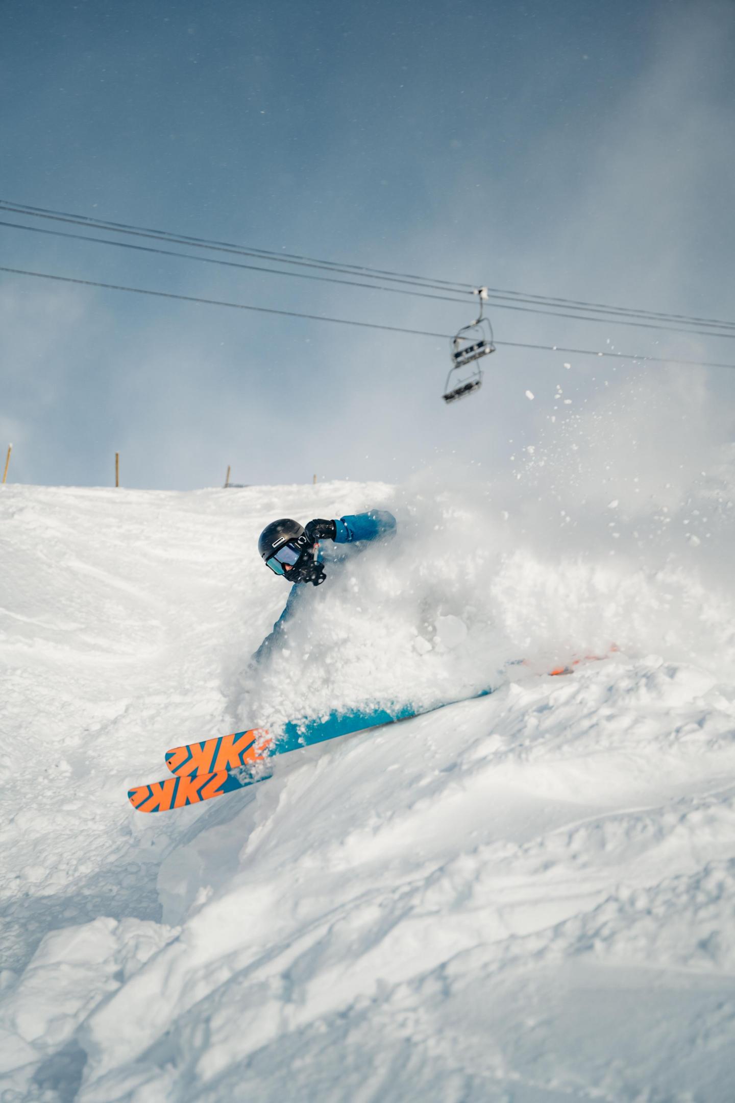 Skier in blue jacket carving through powdery snow.