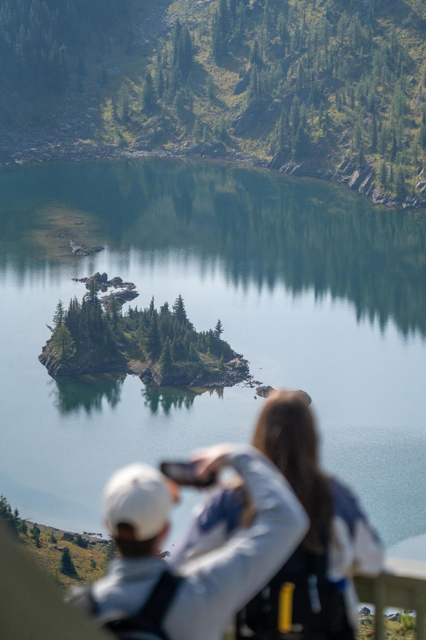 People taking a photo of a scenic mountain lake view.