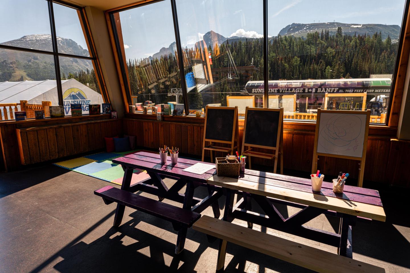 Sunny room with colorful bench, art supplies, and mountain view through large windows.