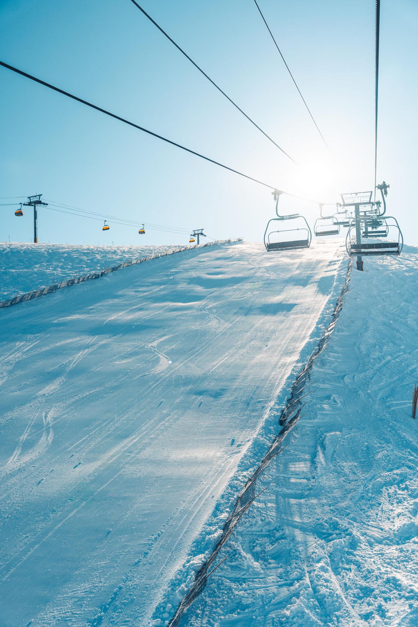 Ski lift ascending snowy slope under bright sun.
