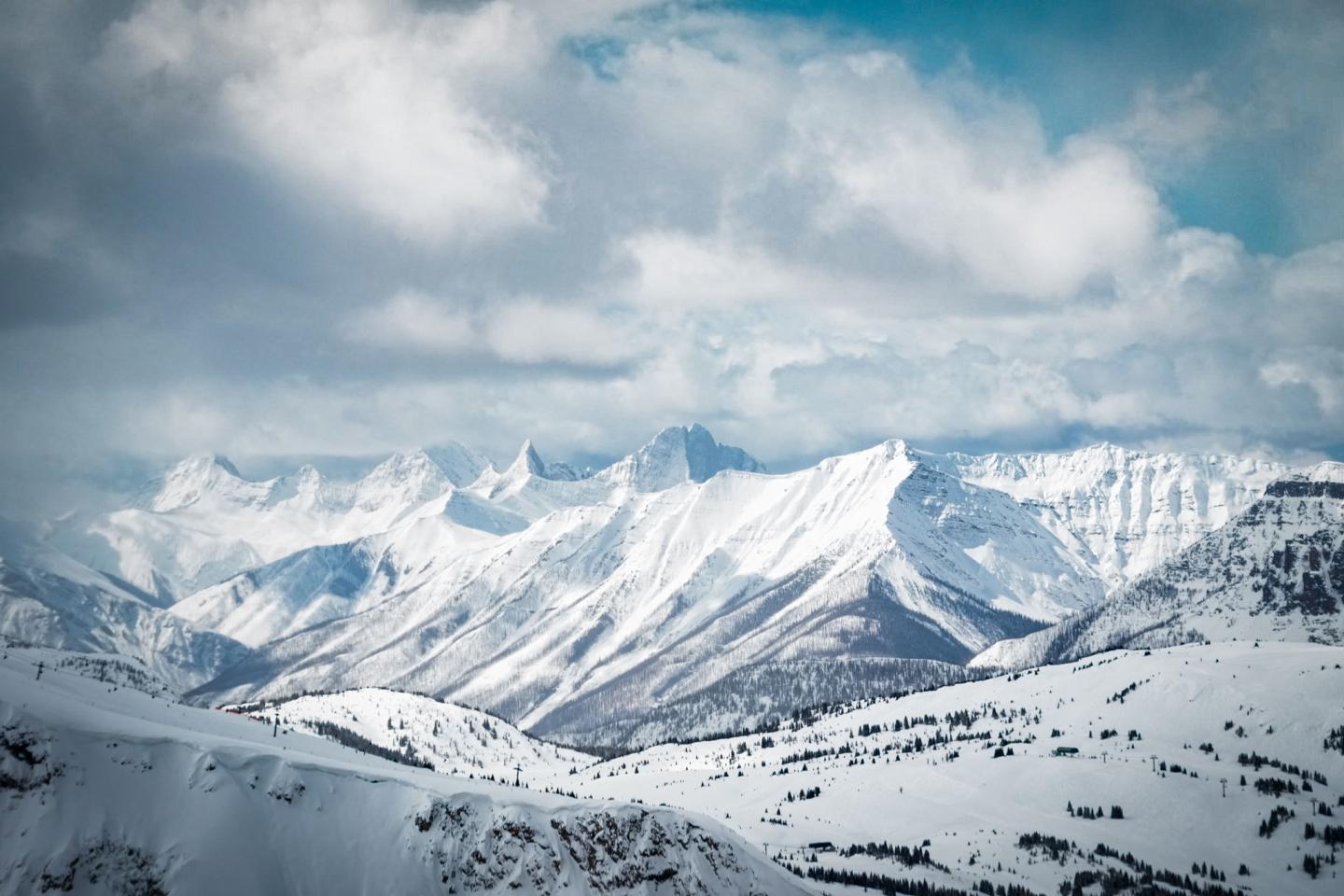Snow-covered mountain range under a cloudy blue sky.