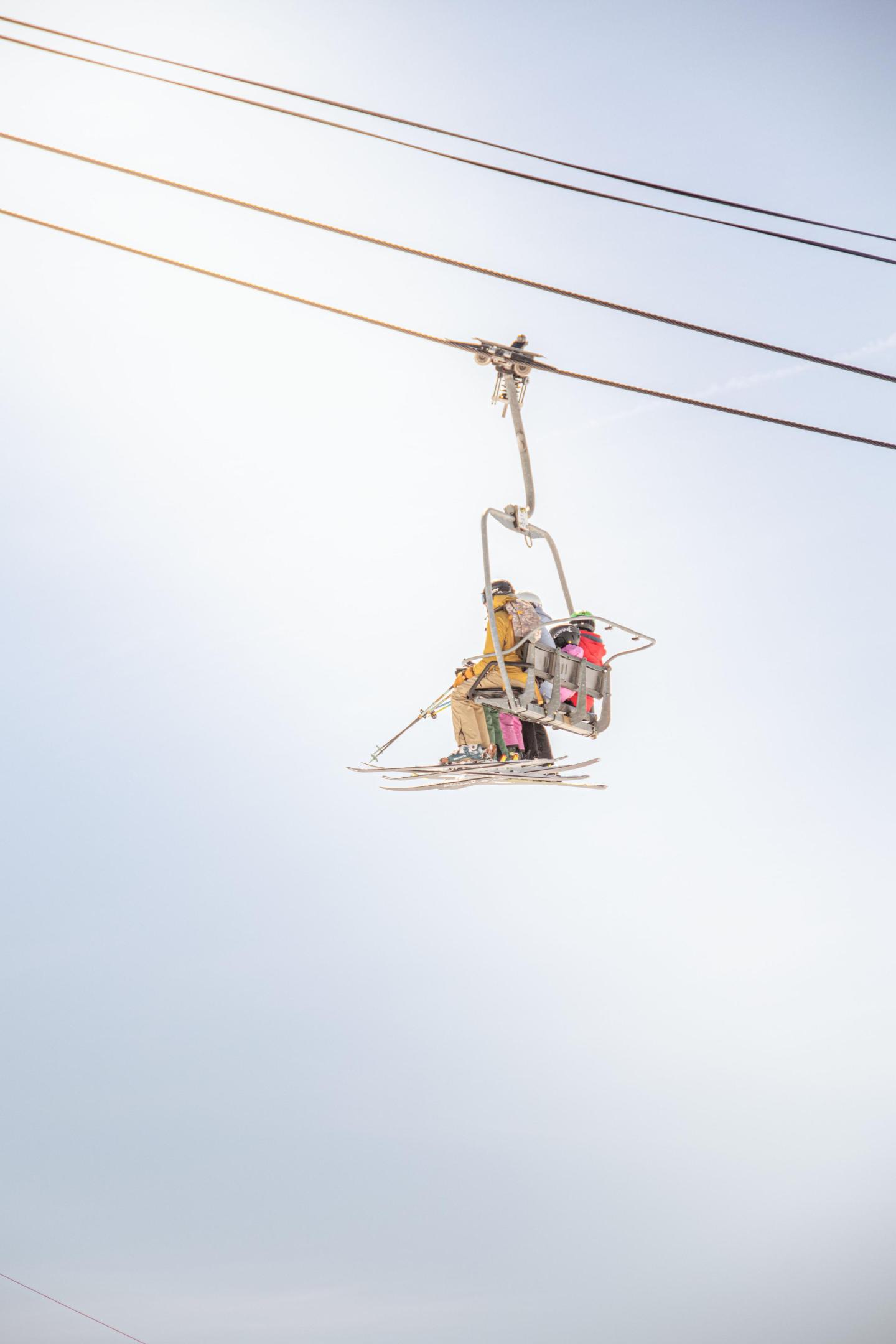 Two people riding a ski lift under a clear blue sky.