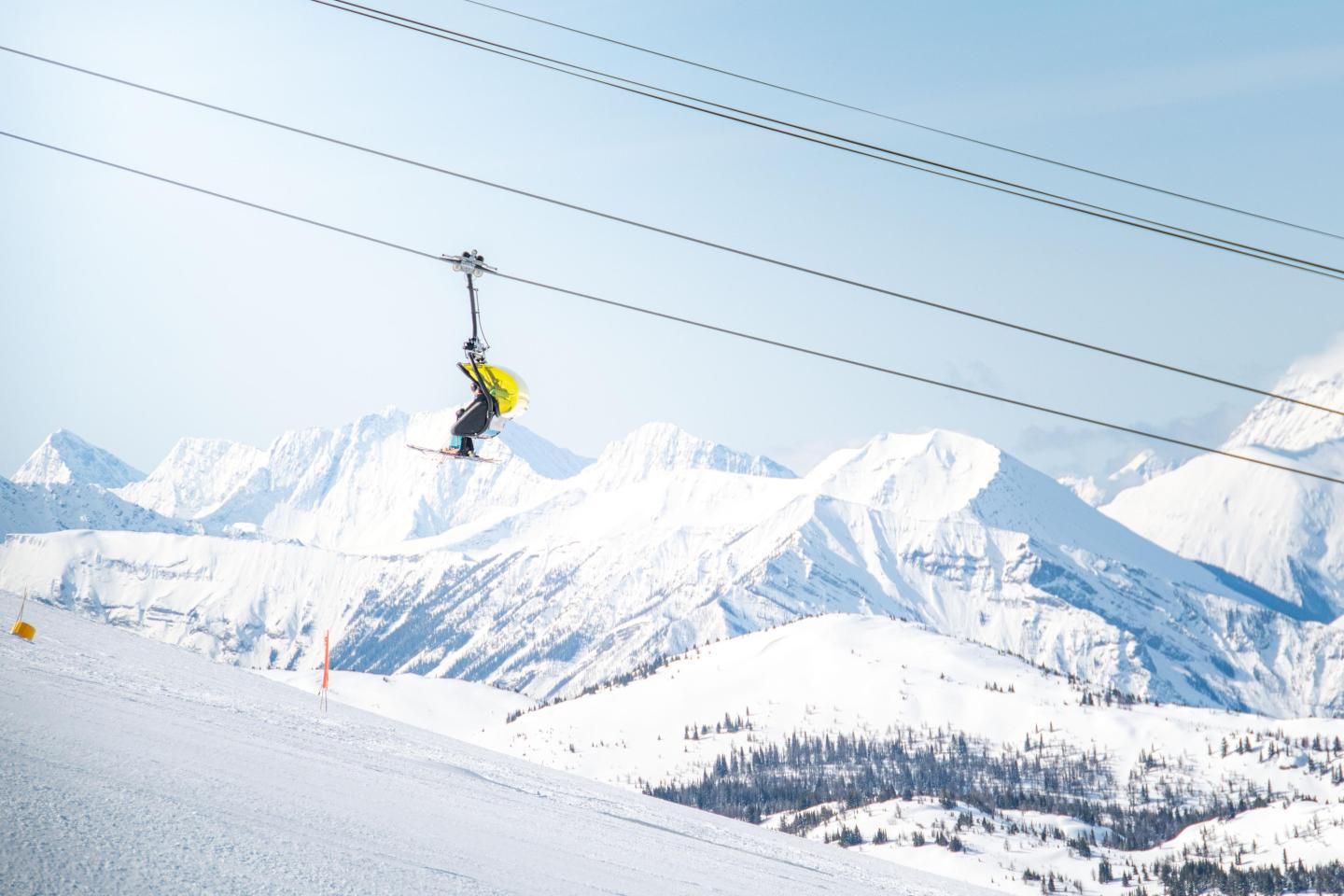 Ski lift with person in yellow jacket, snowy mountain background.
