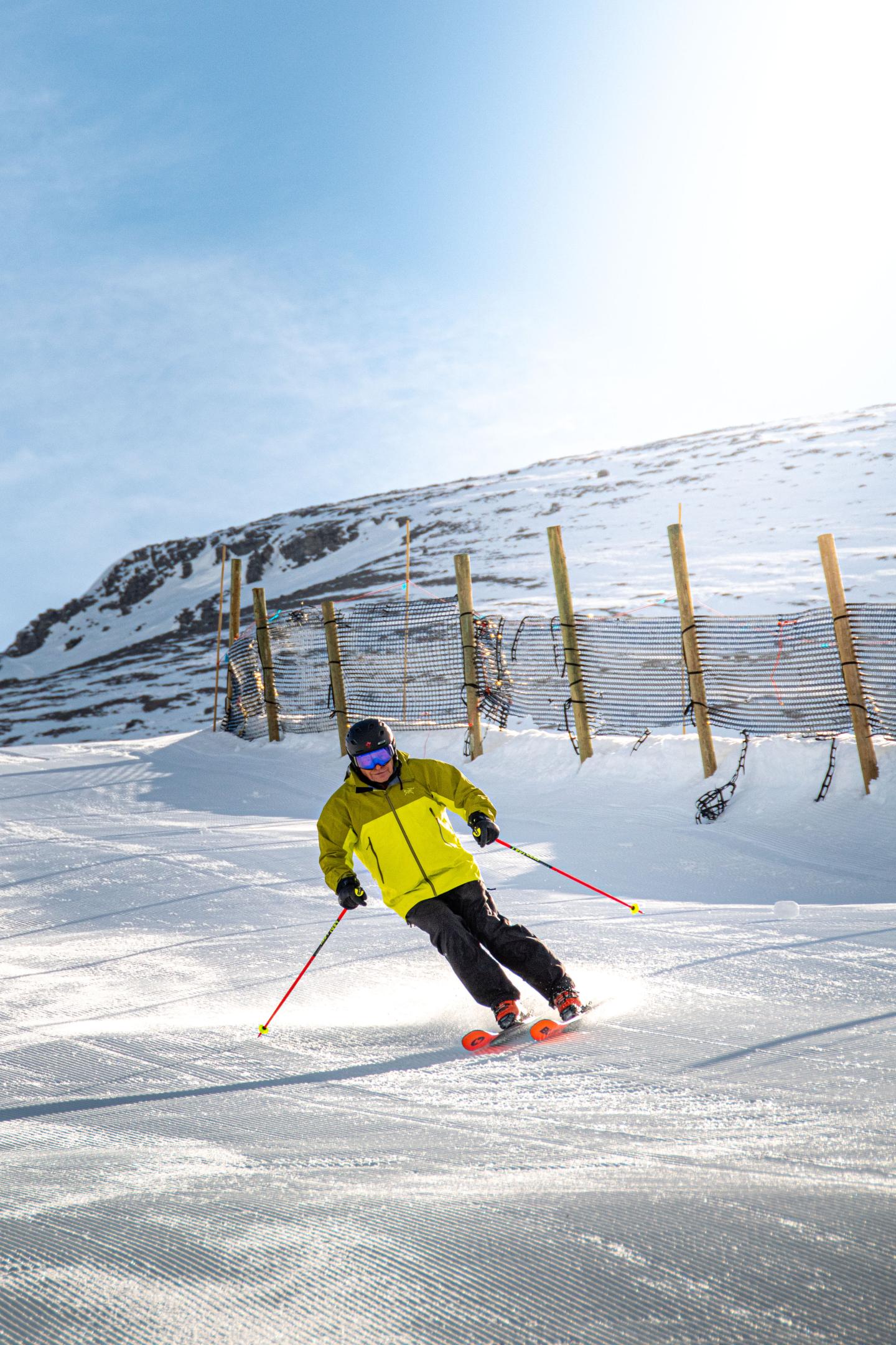Skier in yellow jacket gliding down snowy slope under blue sky.