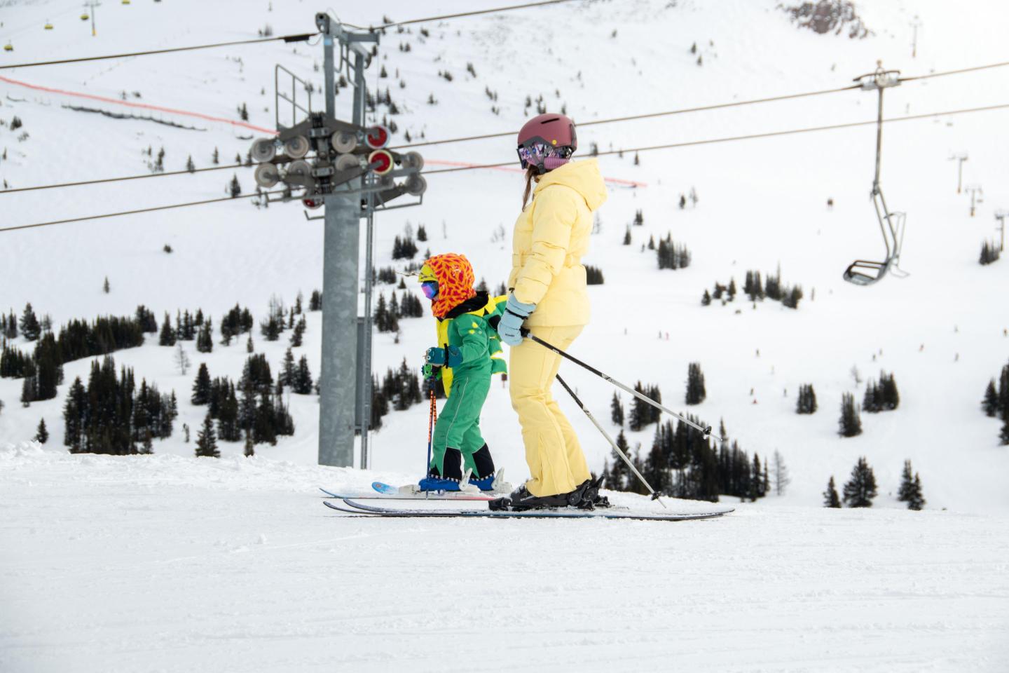 Adult and child skiing on snowy slope near ski lift.