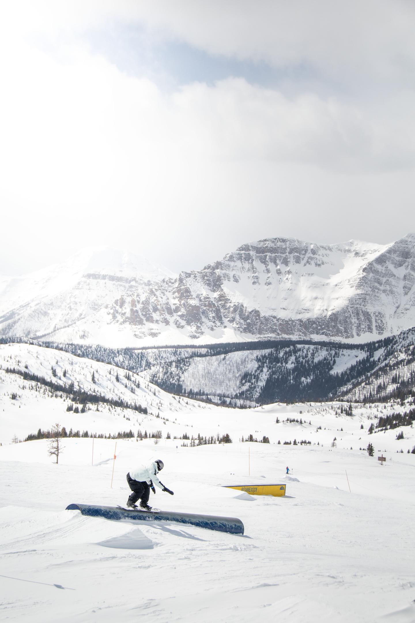 Snowboarder on a rail in a snowy mountain landscape.