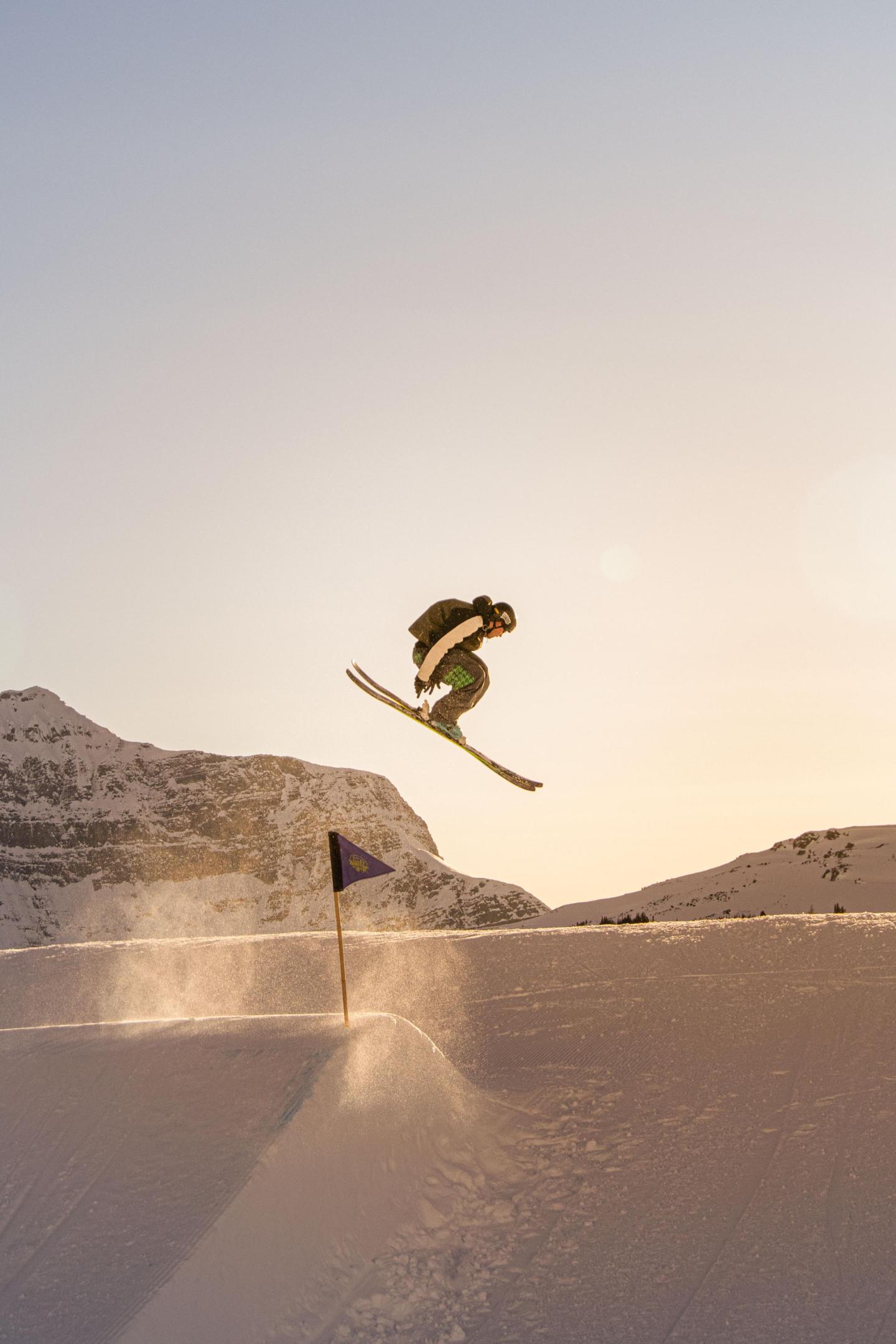 Snowboarder jumping on a snowy slope at sunset.