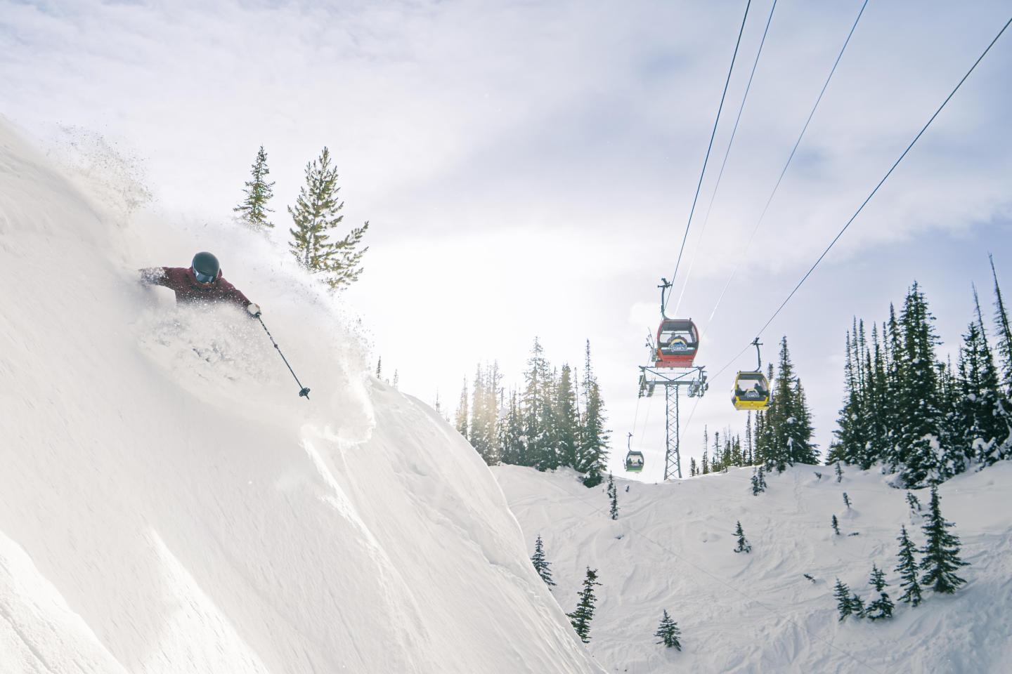 Skier descends snowy slope near gondola lift in a snowy forest setting.