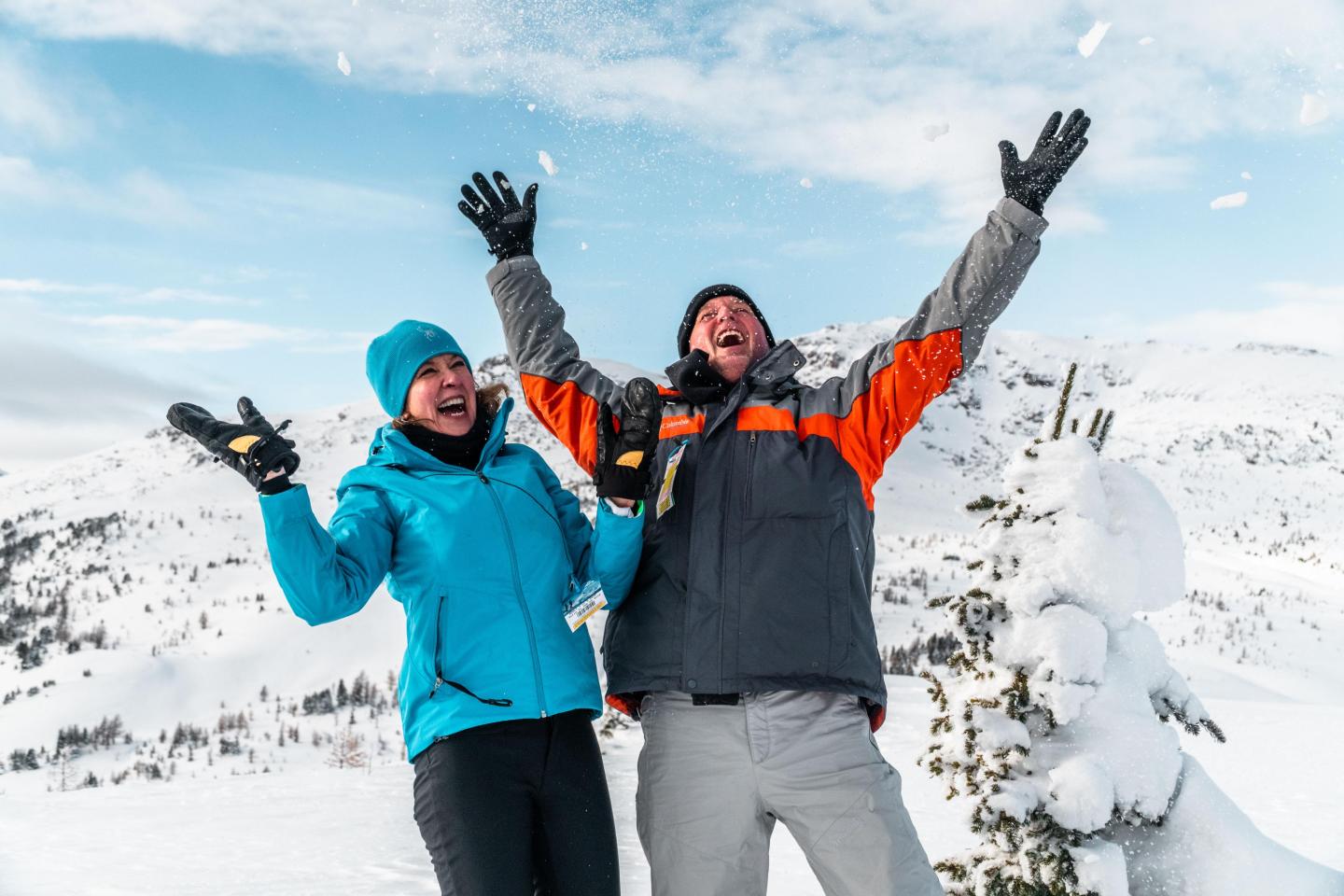 Two people joyfully throwing snow in snowy mountains.