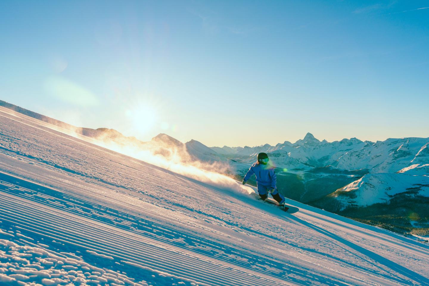 Snowboarder gliding down a sunlit, snowy mountain slope.