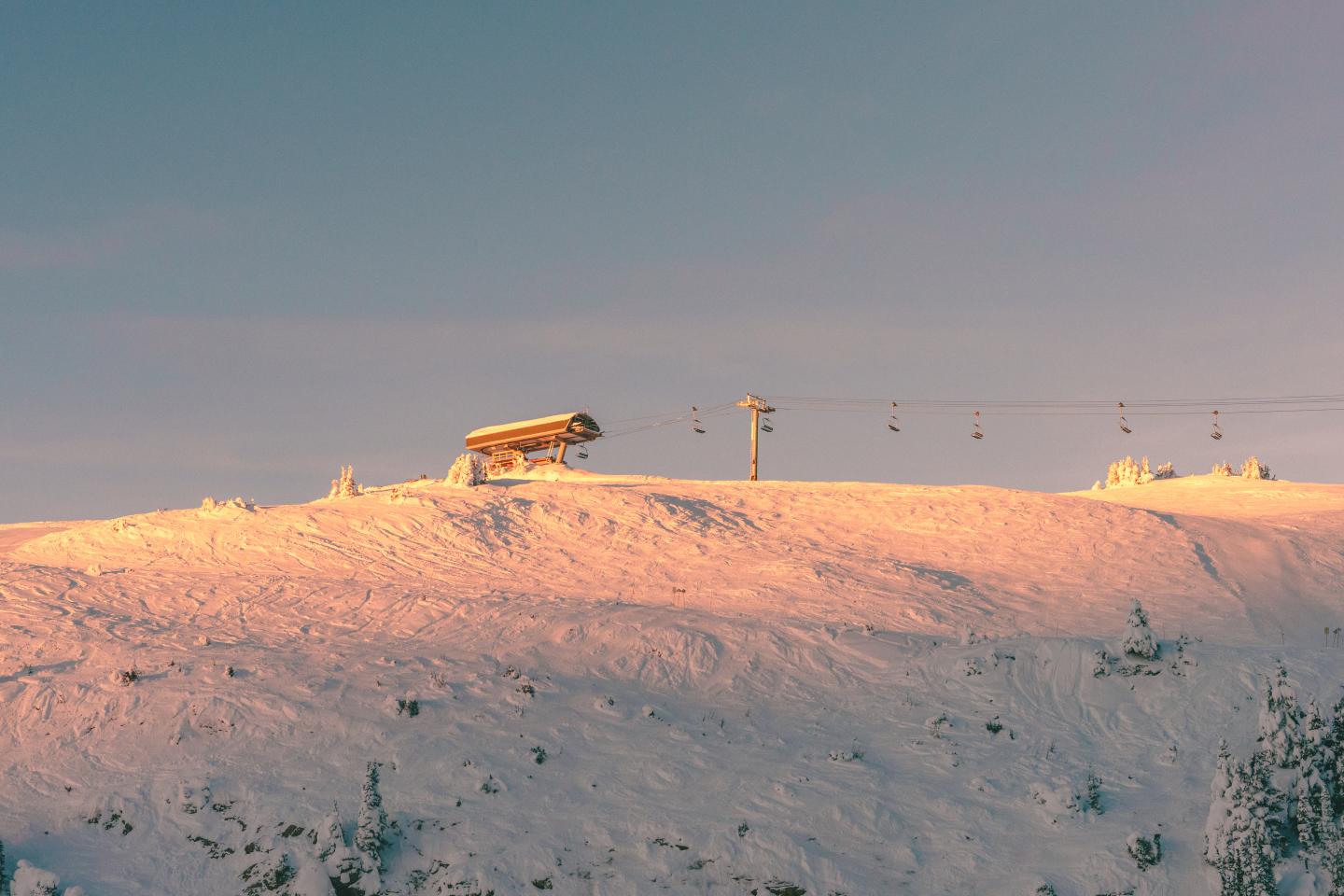 Snow-covered hill at sunset with ski lift silhouetted against the sky.