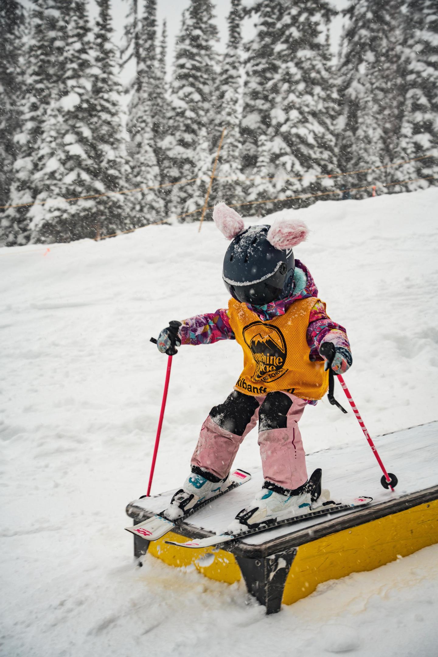Child in bunny ears skiing on snowy slope.