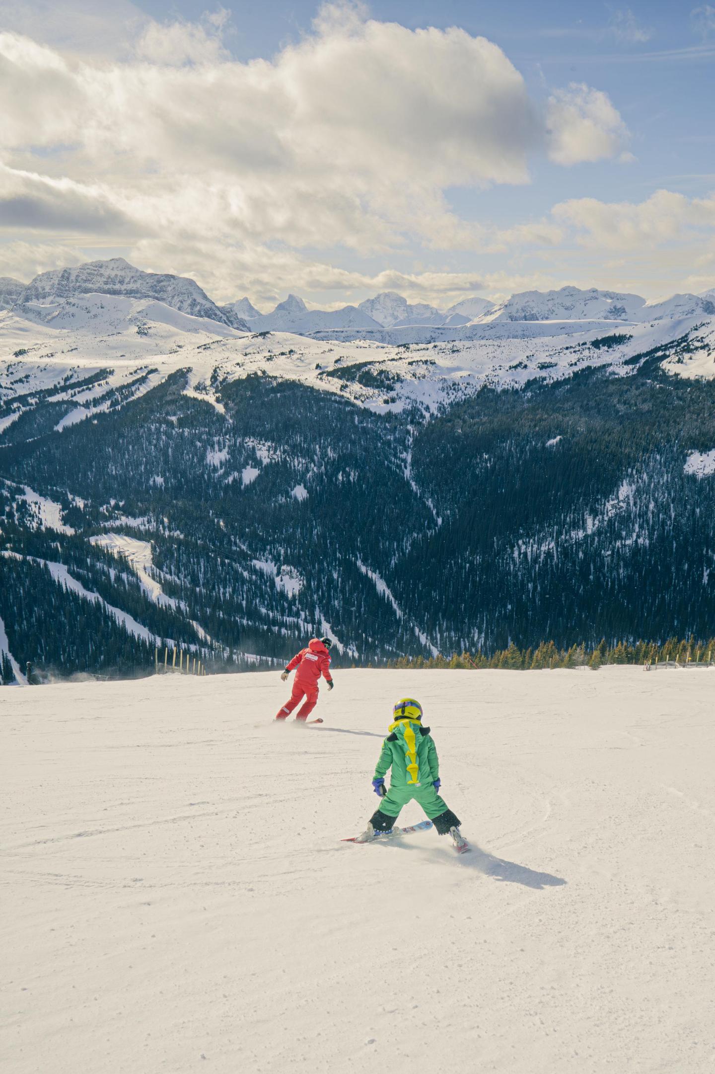 Skiers in colorful outfits on a snowy mountain with a backdrop of snowy peaks.