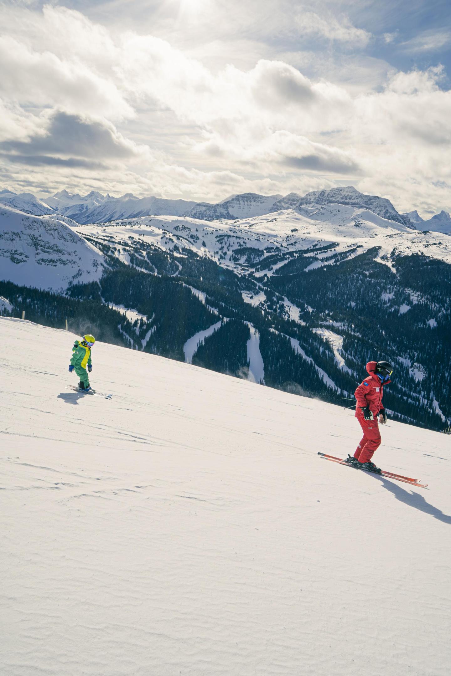Two snowboarders on a snowy mountain slope under a cloudy sky.