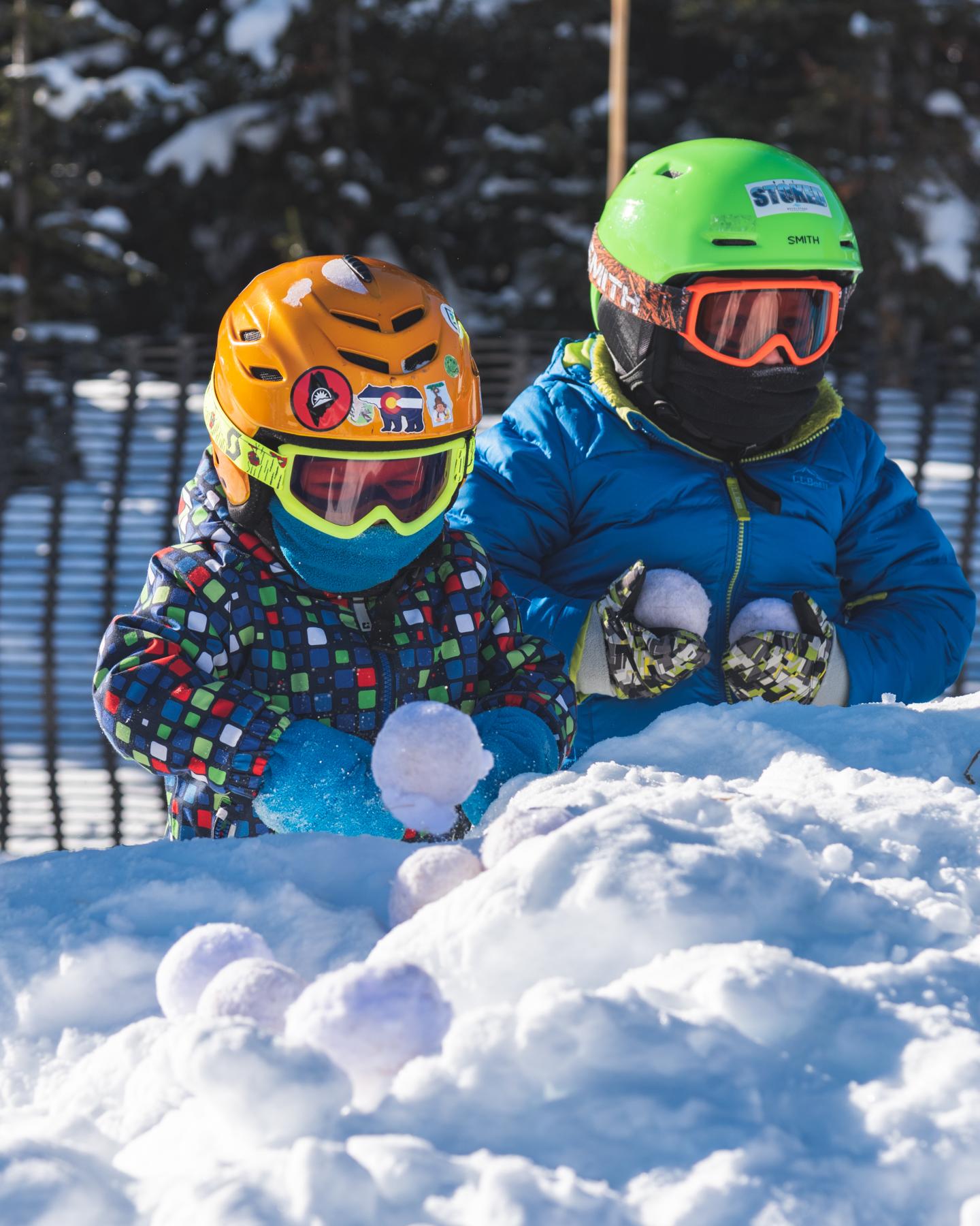 Kids in colorful winter gear making snowballs.