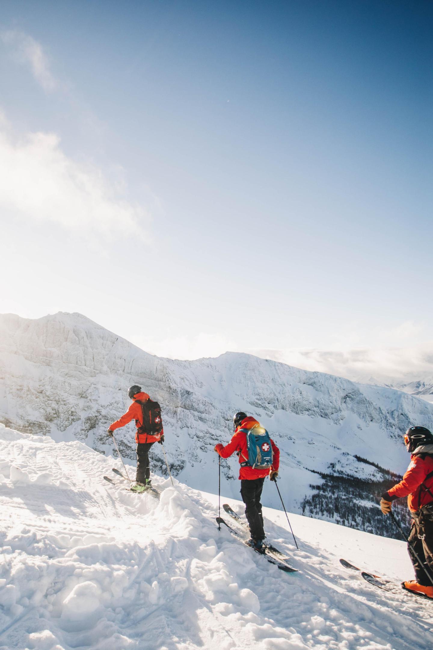Skiers in bright jackets navigating snowy mountain terrain under a clear blue sky.