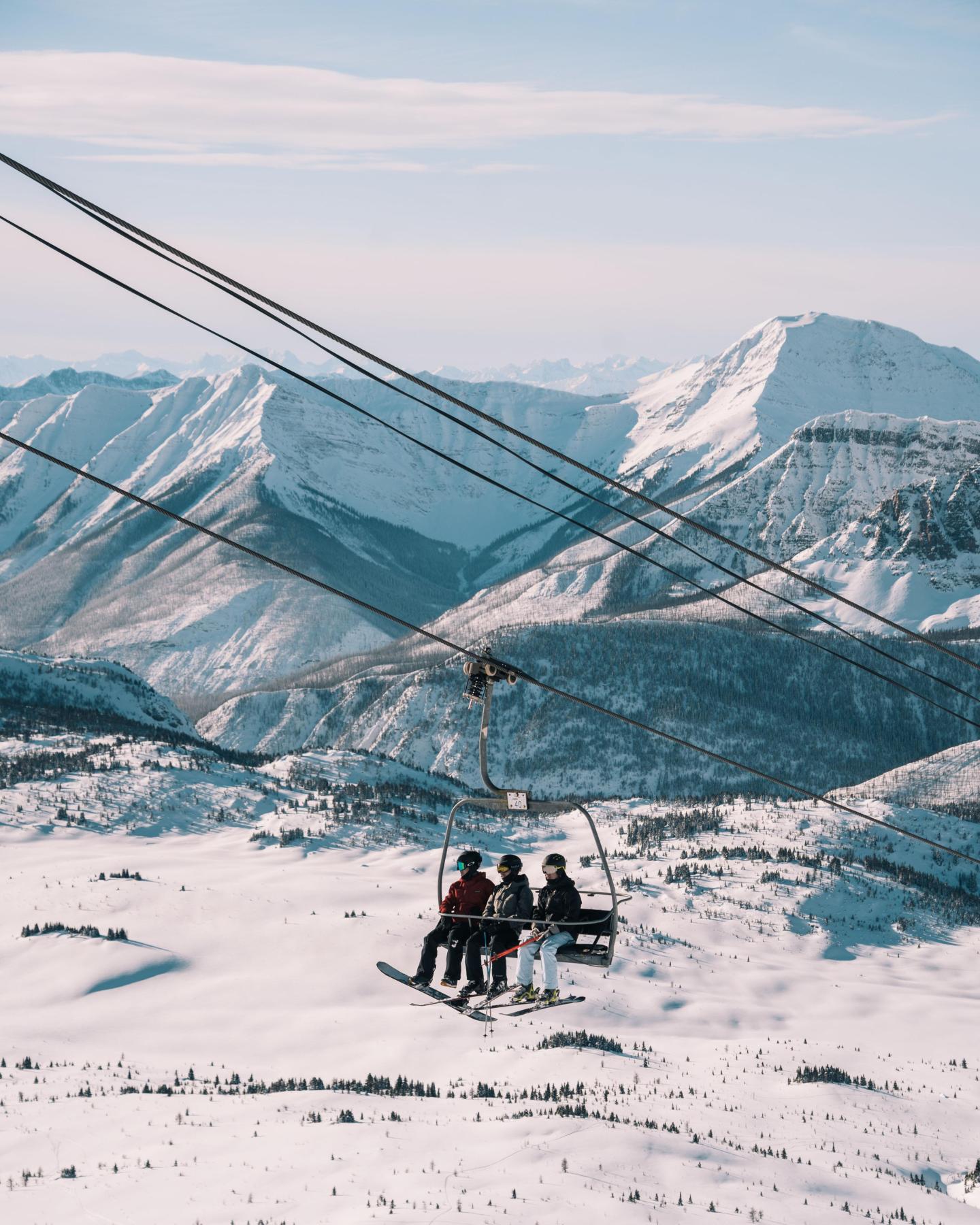 Ski lift with people over snowy mountains.