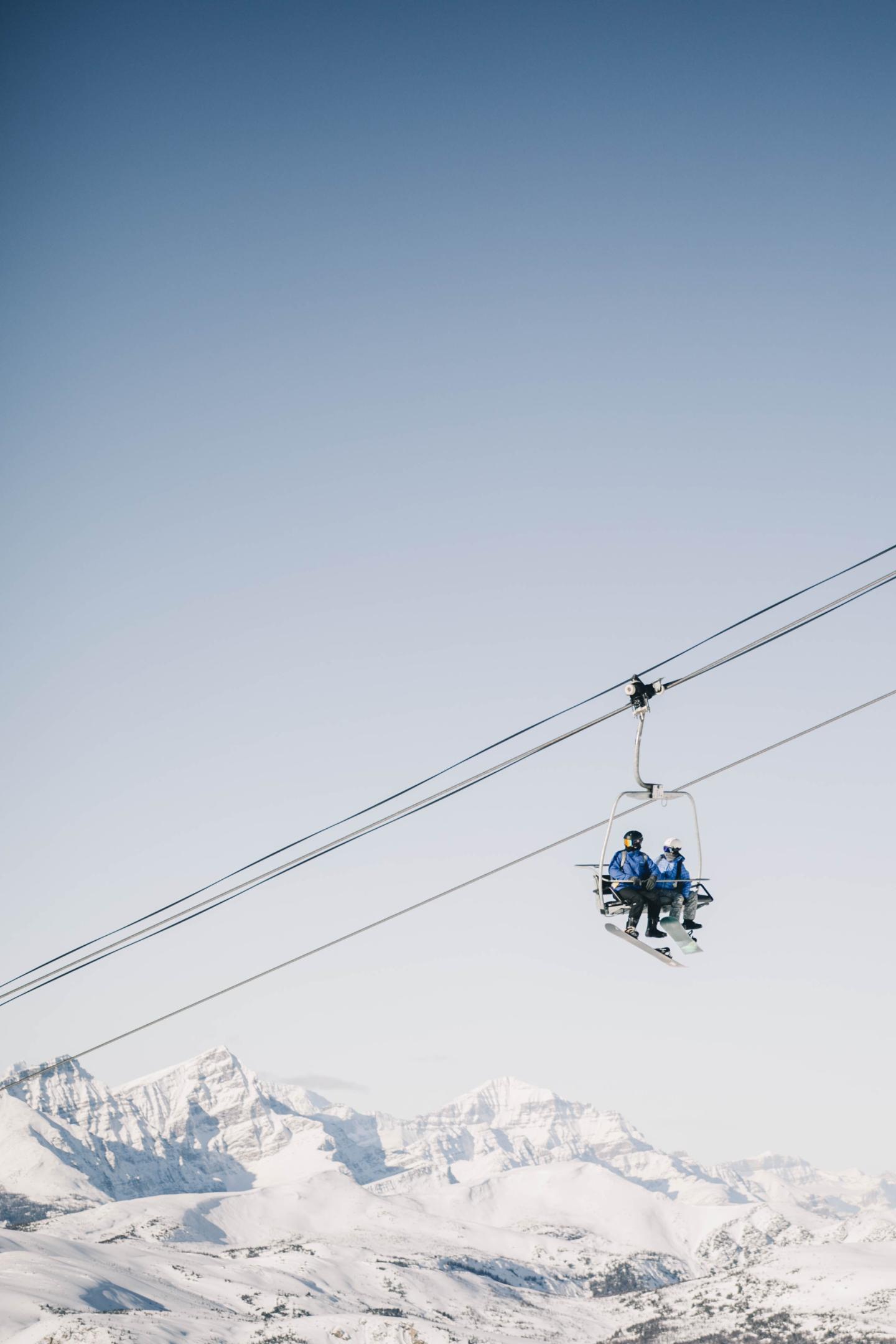 Ski lift with two people over snowy mountains.