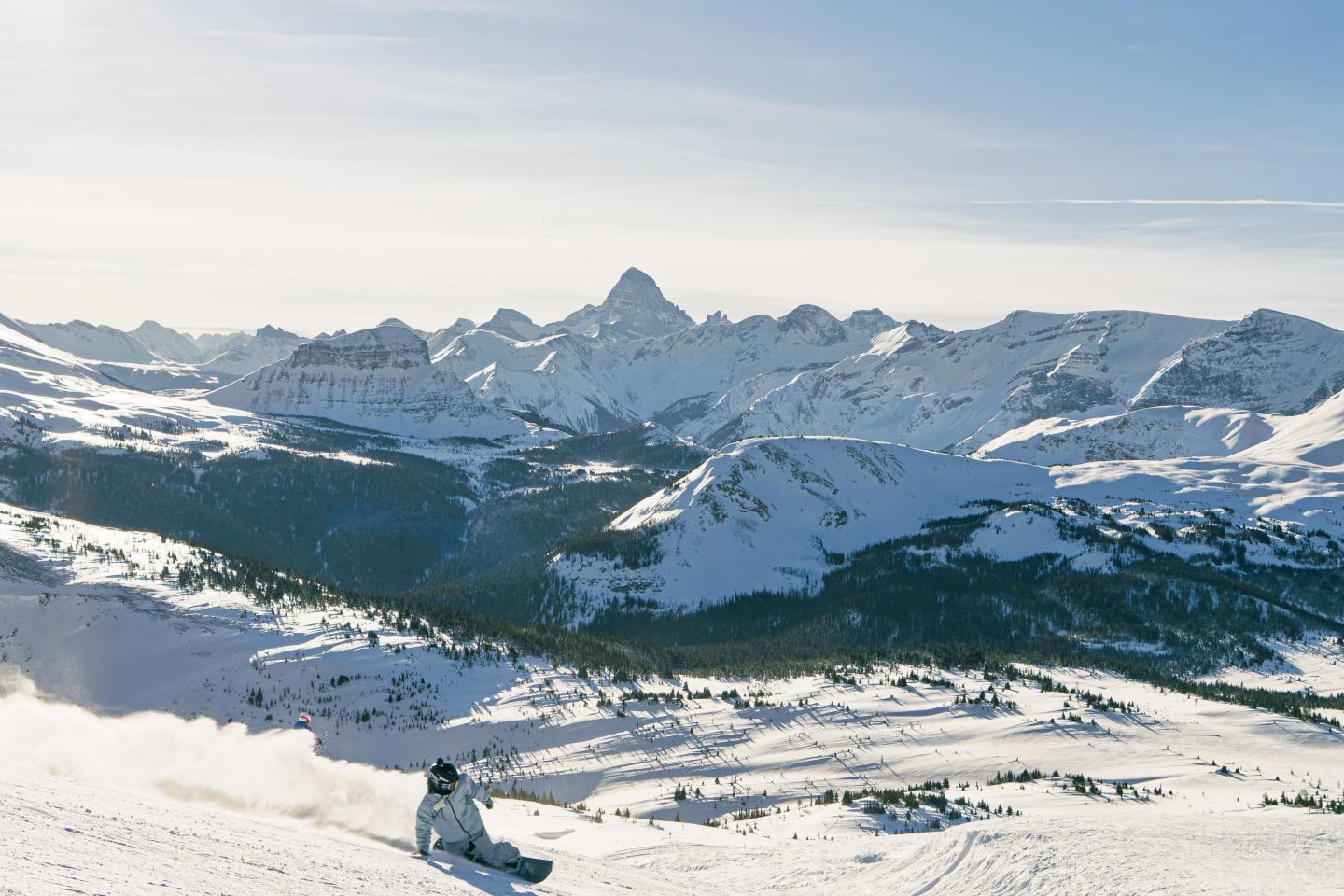 Snowboarder on snowy mountain slope with distant peaks and clear sky.