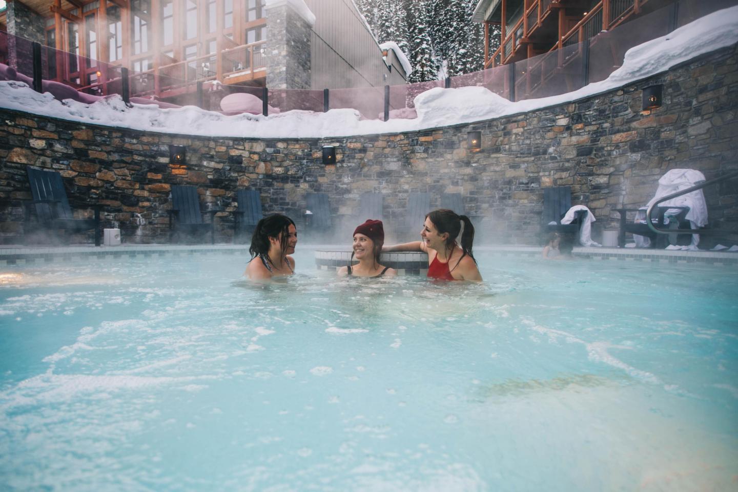Three people enjoying a hot tub in a snowy outdoor setting.