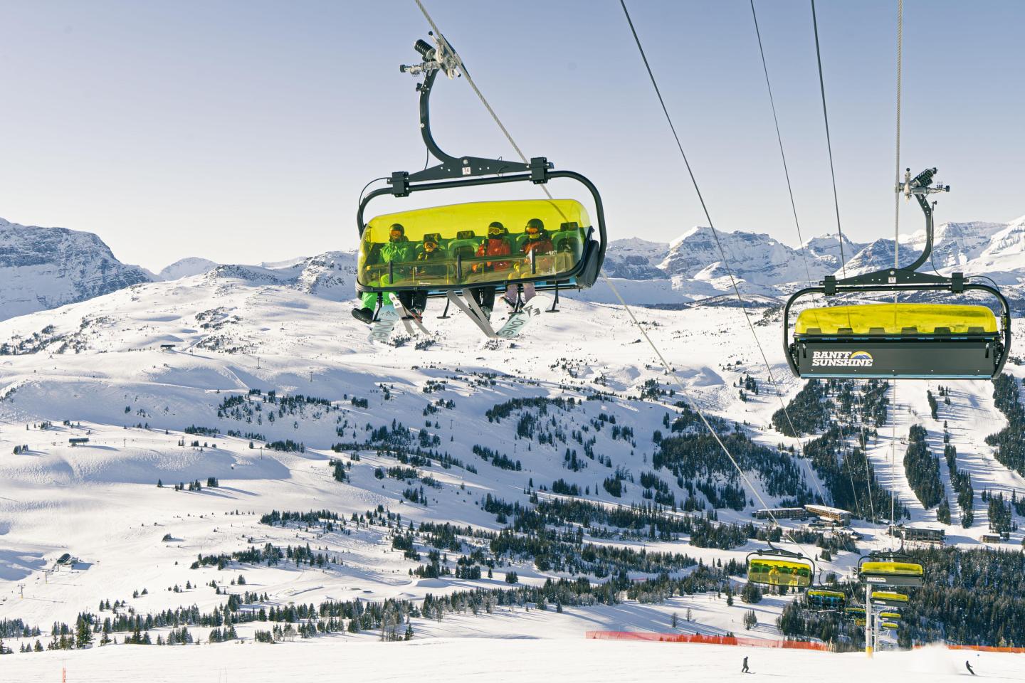 Two ski lifts with people over snowy mountains.