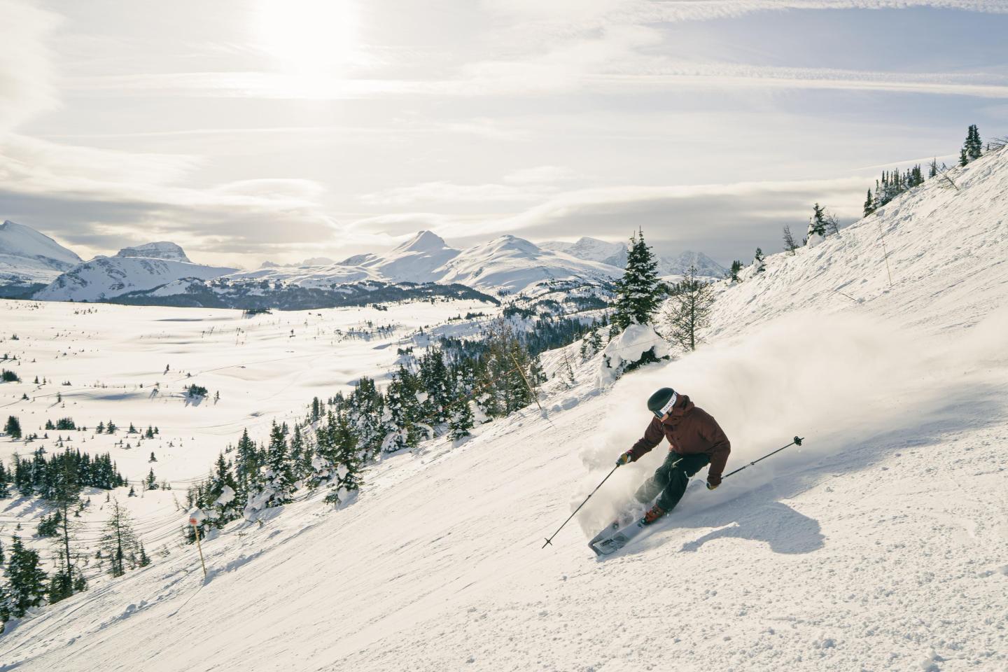 Skier carving down a snowy slope, mountains in the background.