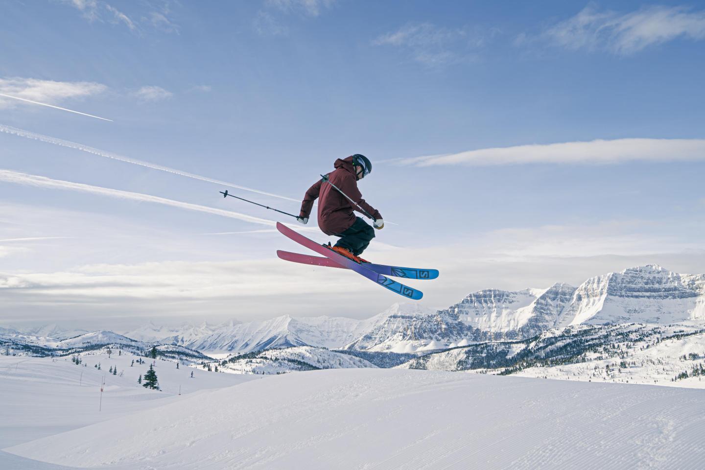 Skier in mid-air against snowy mountain landscape.
