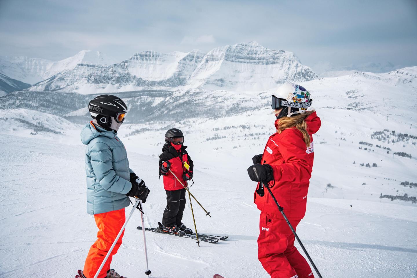 Three skiers in colorful gear stand on a snowy mountain slope.