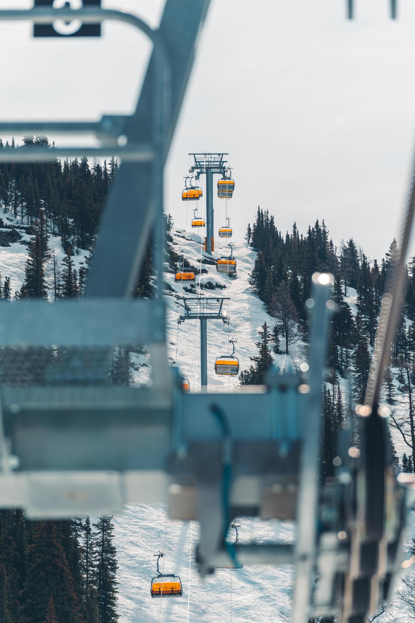 Ski lift with yellow gondolas over snowy mountains and pine trees.