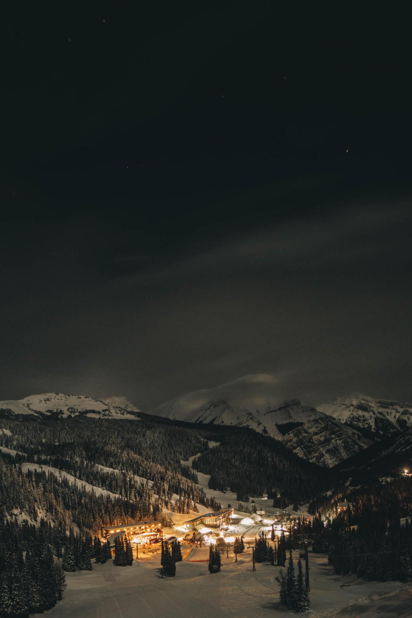 Snowy village illuminated at night, nestled in a mountainous landscape.