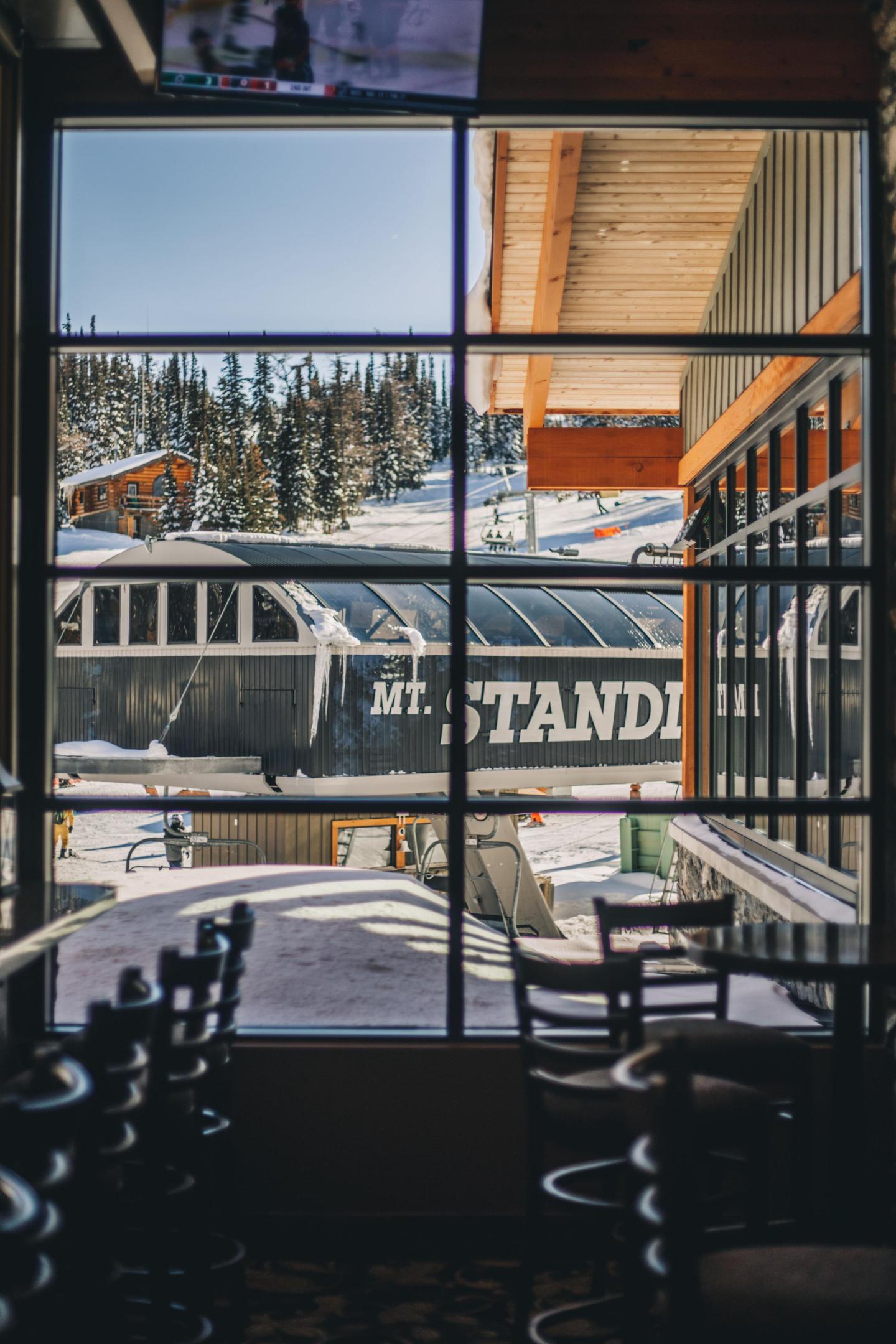 Ski lift and snowy trees seen through a window from a cozy cafe.