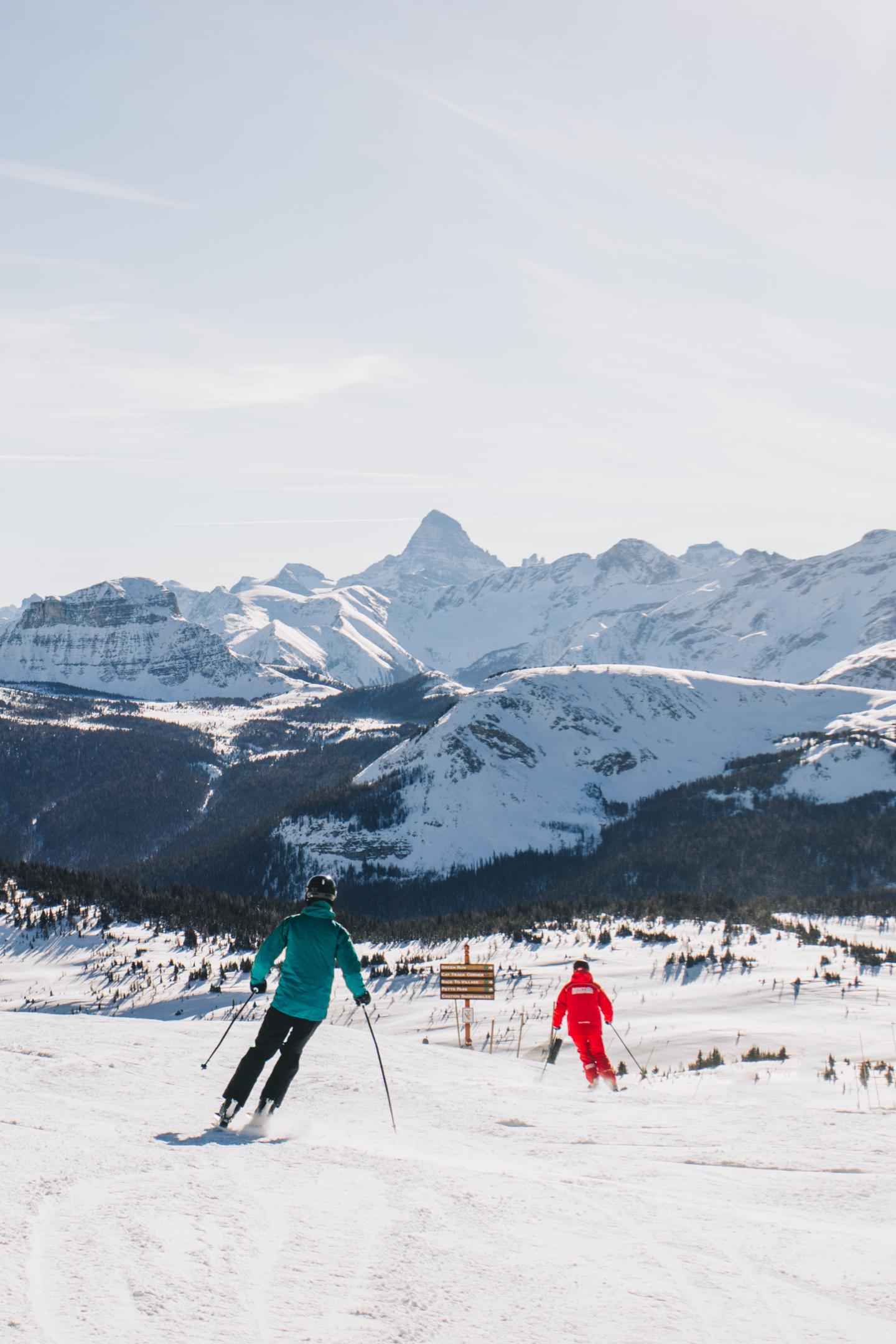 Skiers on snowy slope with mountain range backdrop.