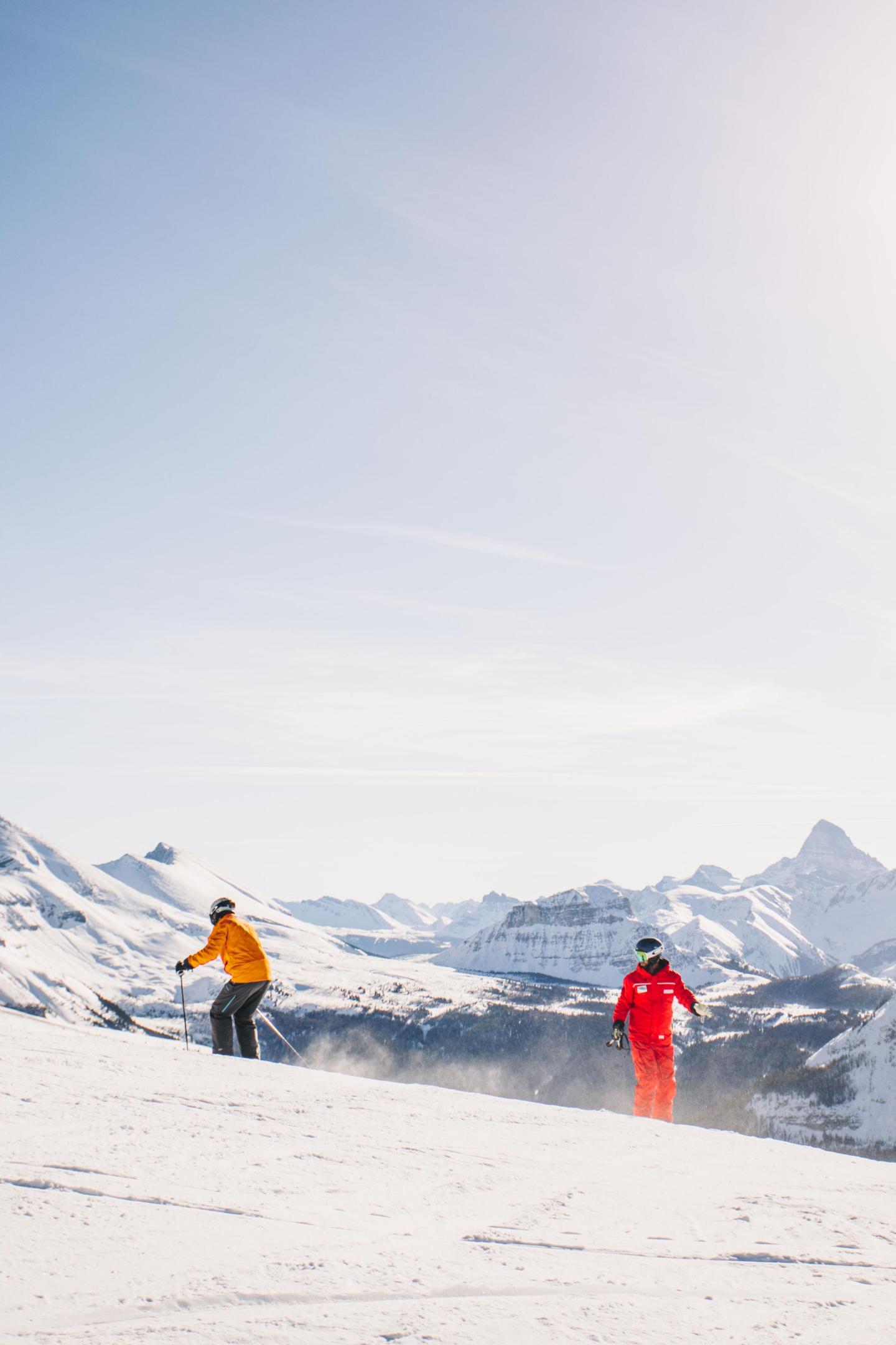 Skiers in bright outfits on a snowy mountain slope under a clear sky.