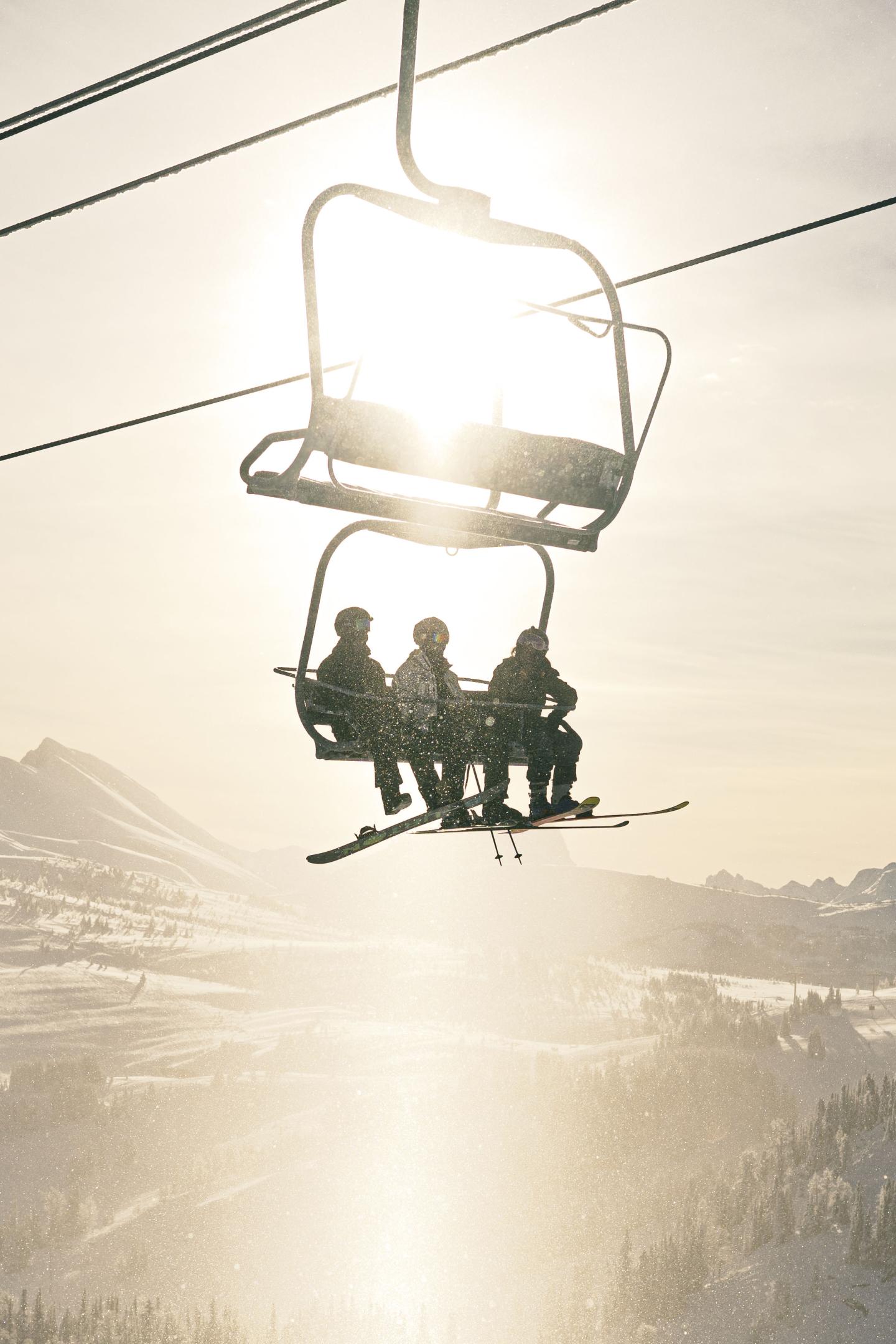 Three people on a ski lift silhouetted against the sun.