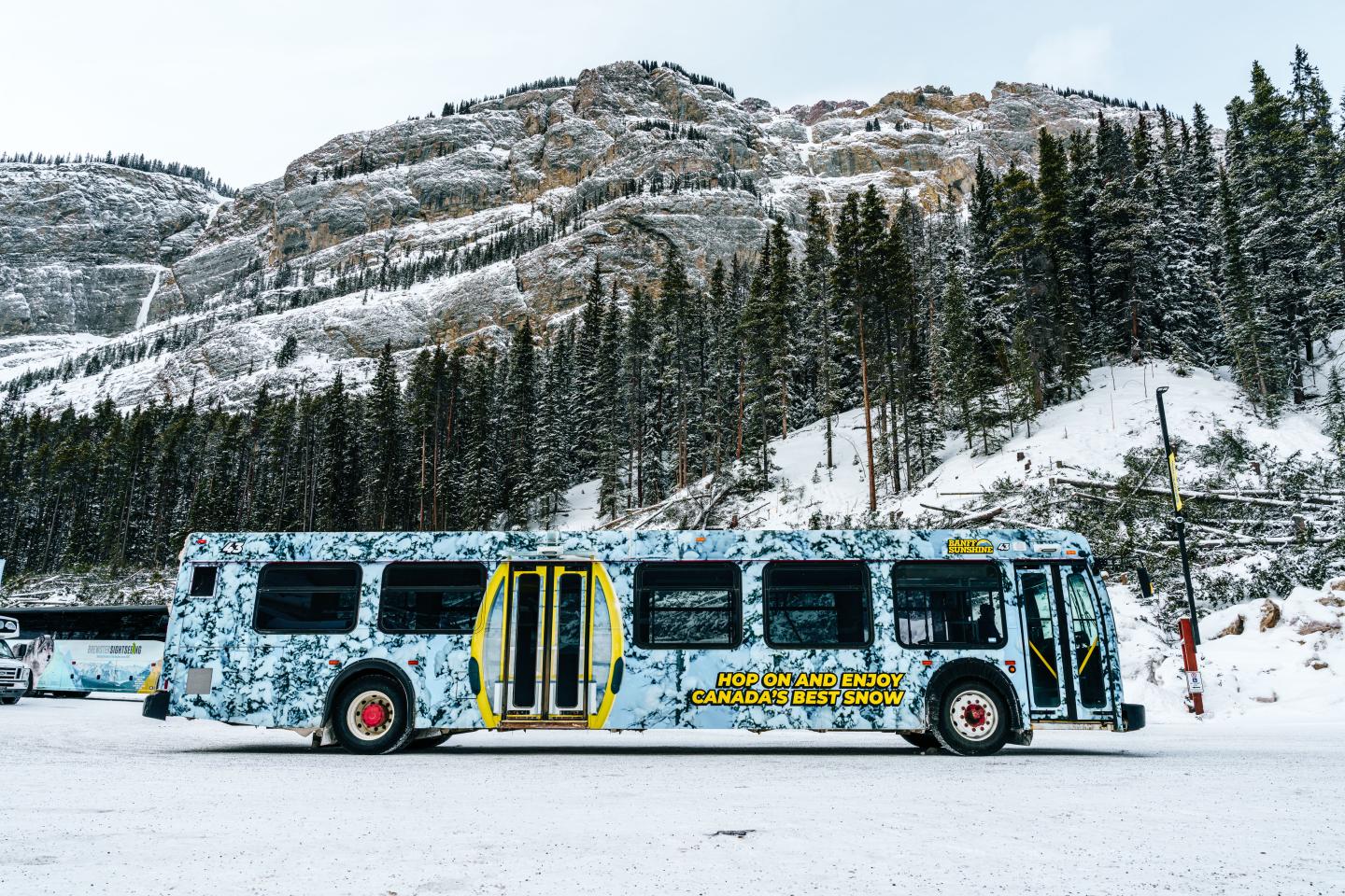 Bus on snowy landscape with mountain and trees in background.