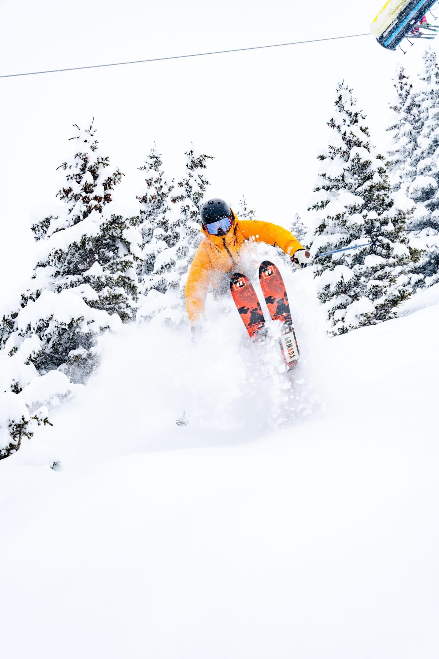 Skier in orange jacket jumps on snowy slope, surrounded by frosted trees.