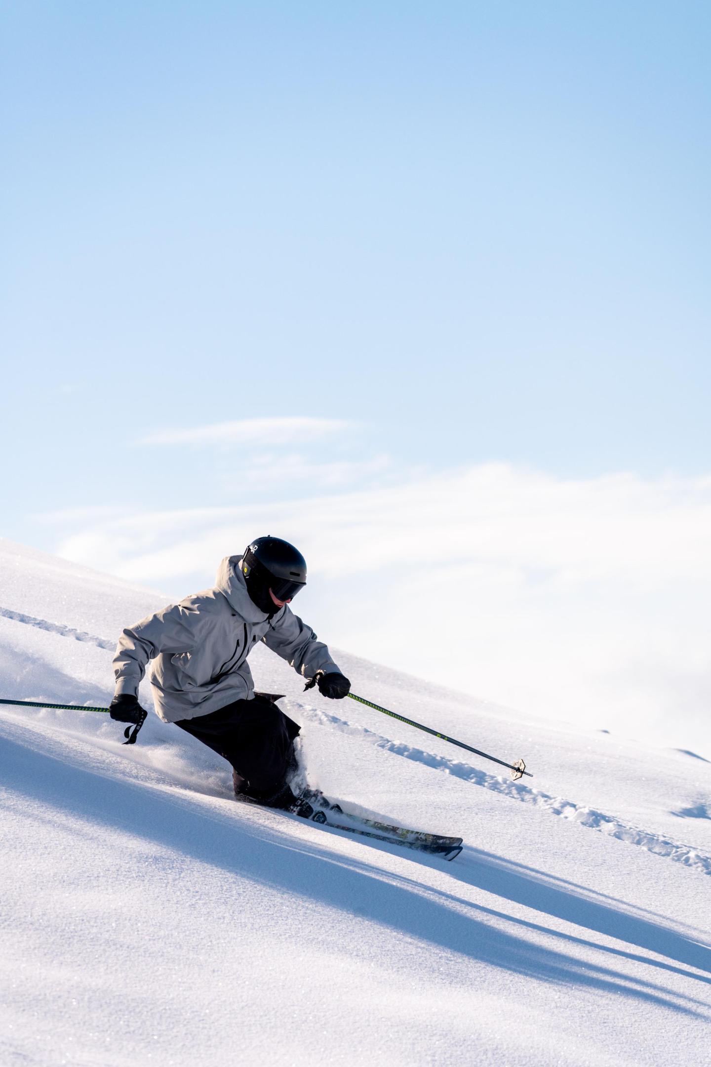 Skier in white jacket on snowy slope under clear blue sky.