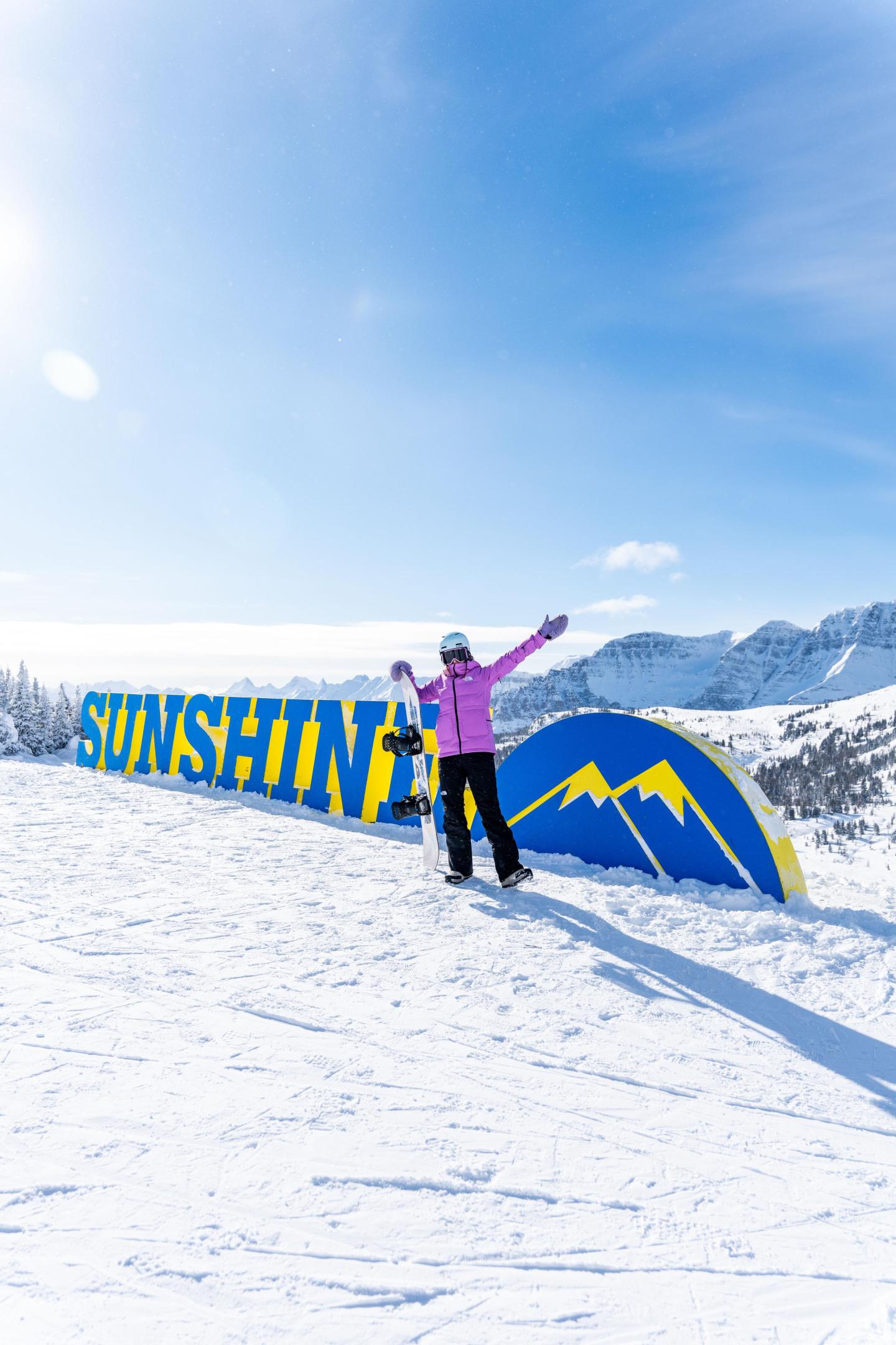 Person in pink jacket posing on snowy slope under blue sky.