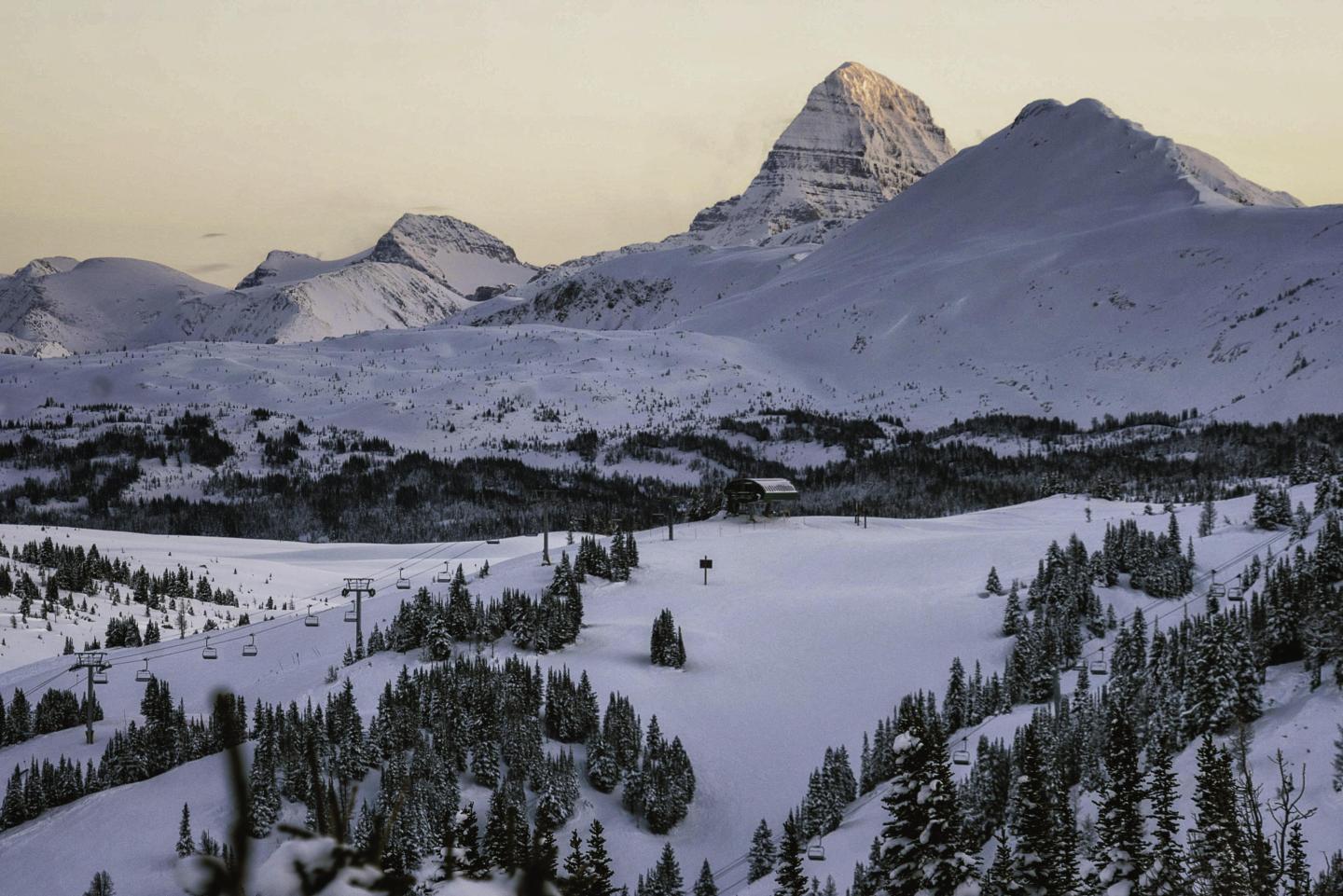Snow-covered mountains and evergreen trees at sunset.