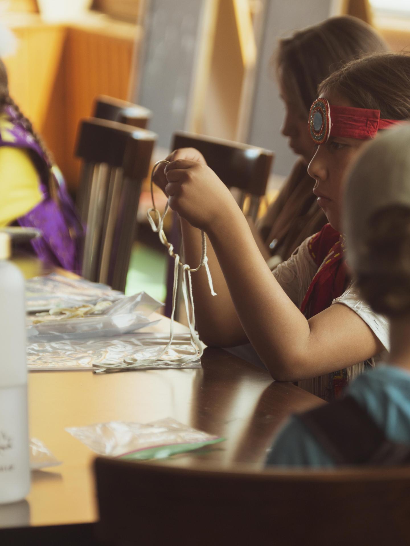 Children crafting with beads at a table in a sunlit room.