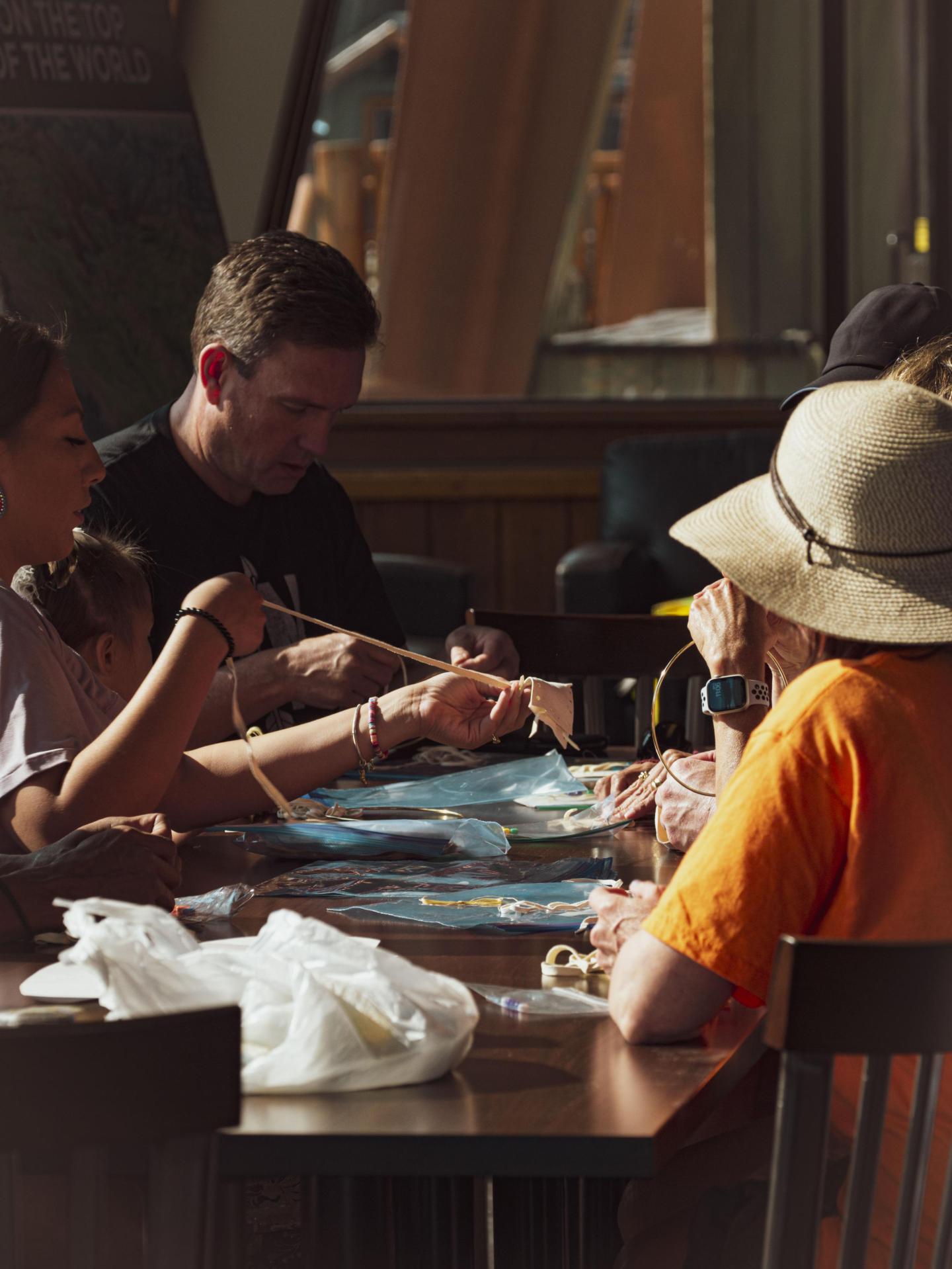 Group crafting at a table, warmly lit, person in straw hat visible.