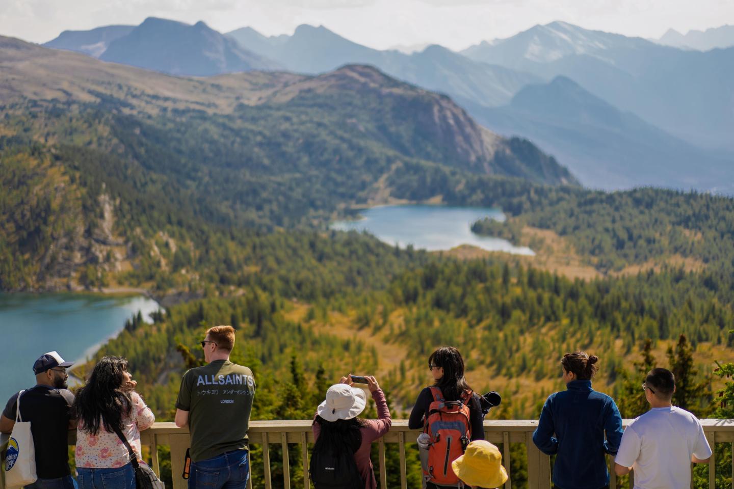 People enjoying a scenic mountain view with lakes and forests.