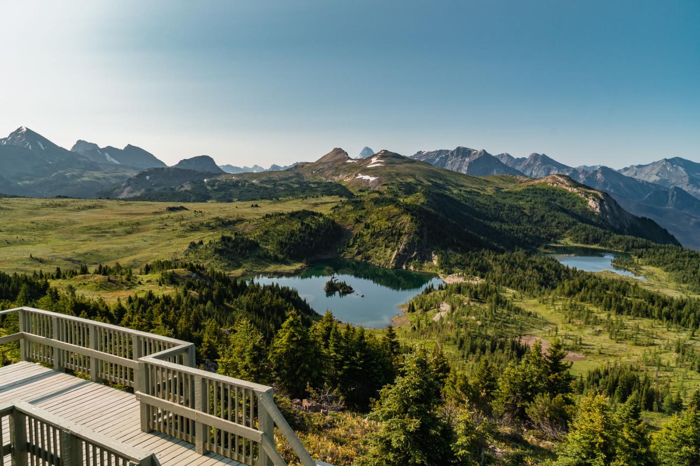 Mountain landscape with lakes, greenery, and a wooden observation deck.